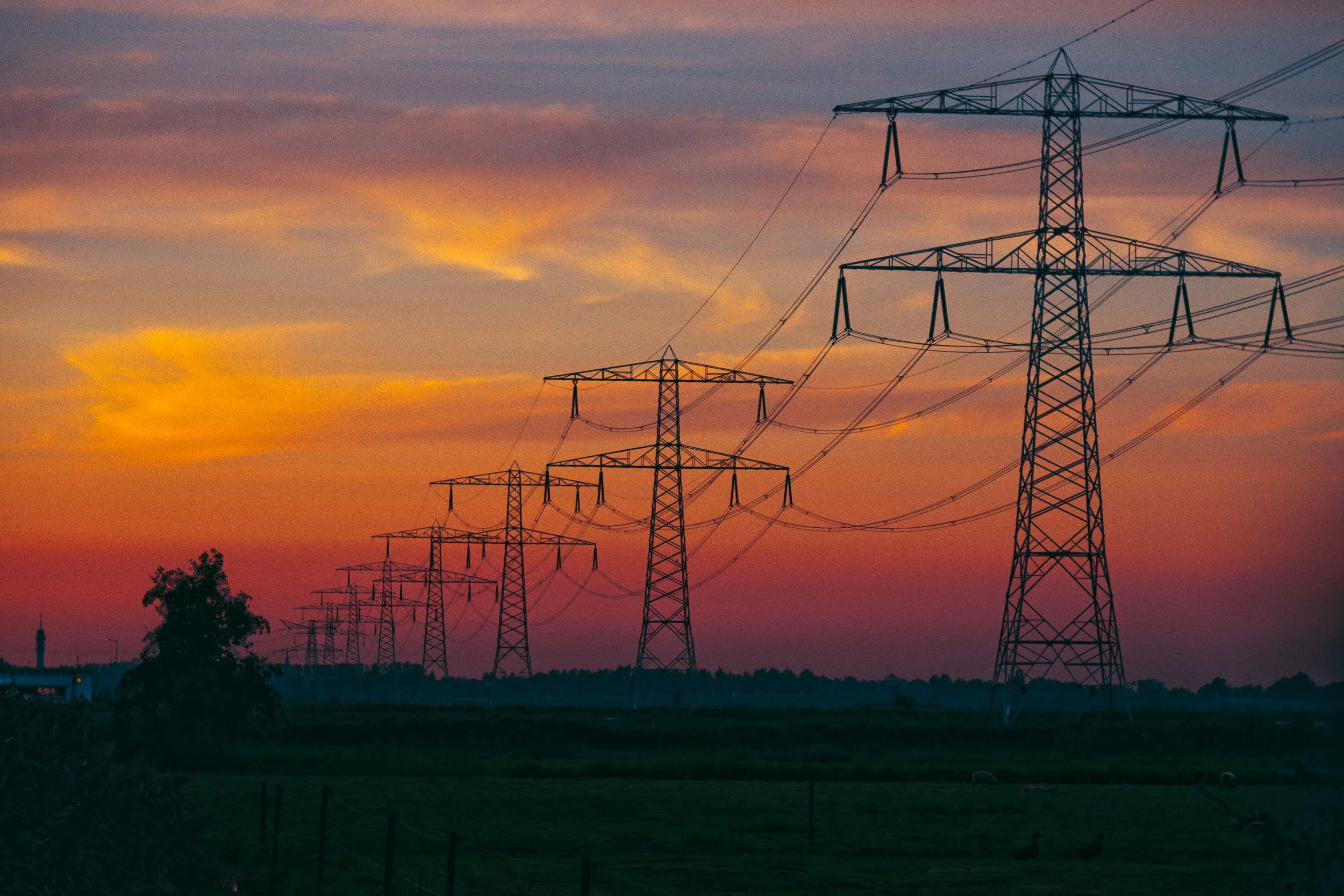Lijn met hoogspanningsmasten onder een kleurrijke zonsondergang.