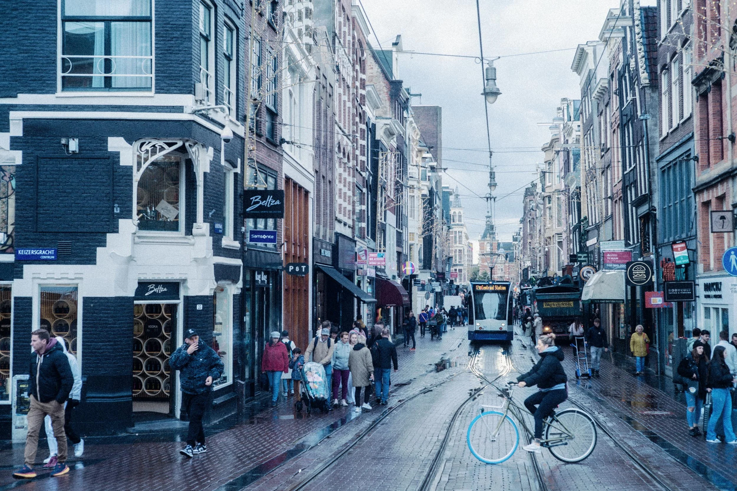 Straatbeeld in een Europese stad met tram, mensen, winkels en natte bestrating, waarschijnlijk na regen.