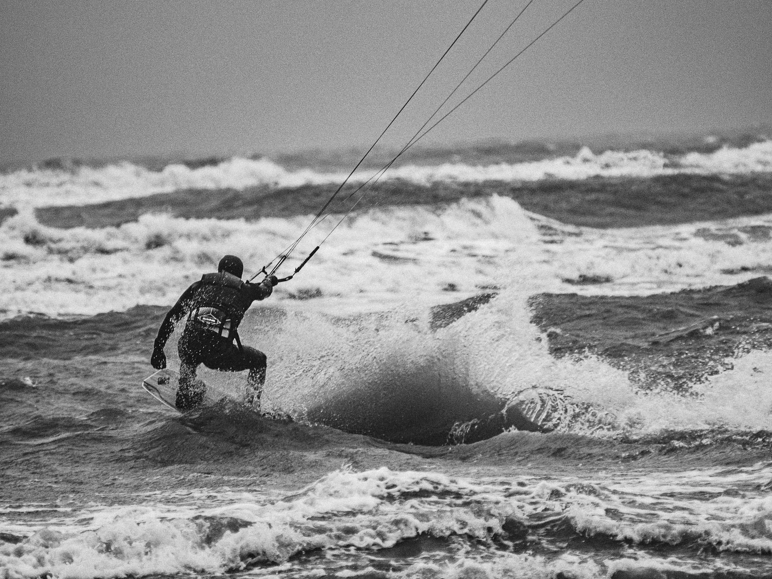 Een surfer die op zee een sprong maakt met het golvend water rondom hem in zwart-wit.
