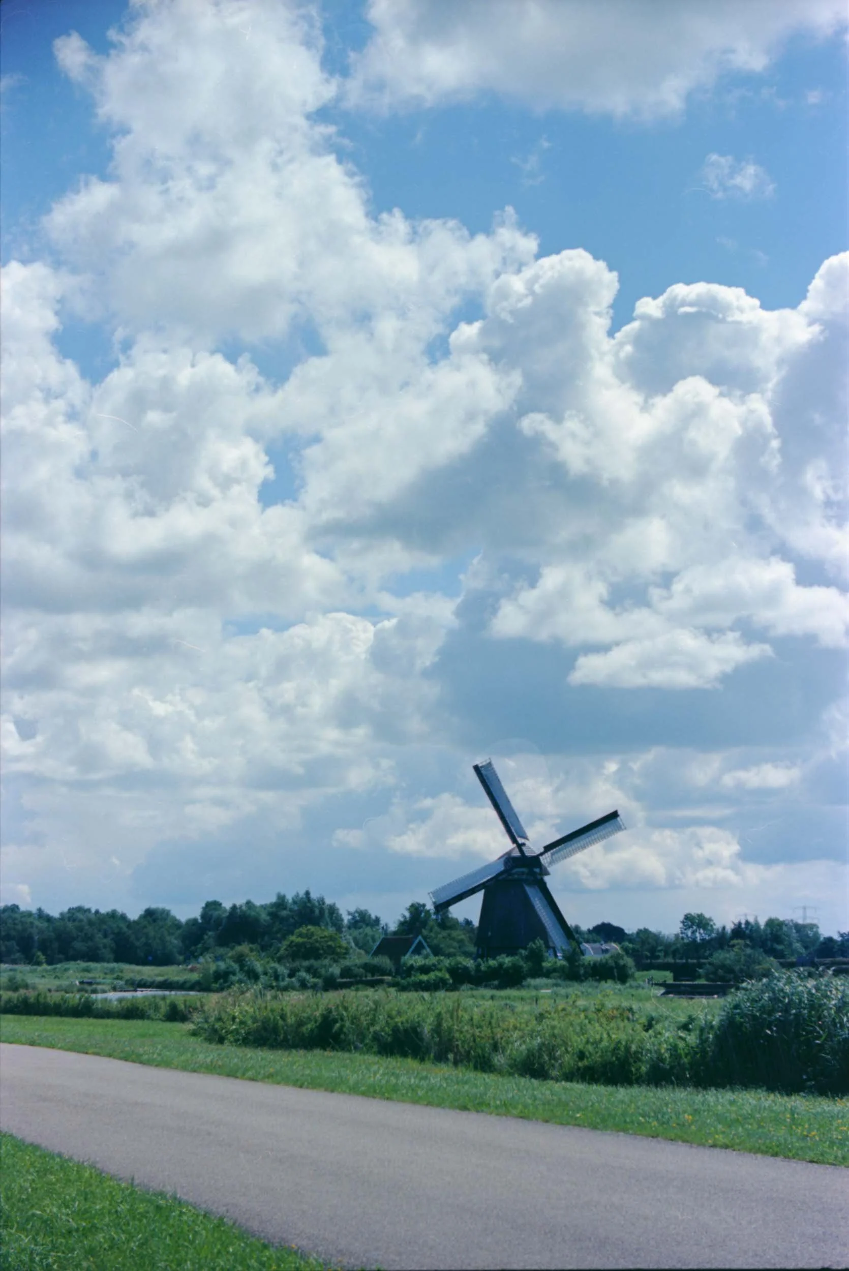 Een schilderachtig landschap met een klassieke windmolen op groene weilanden onder een bewolkte blauwe hemel.