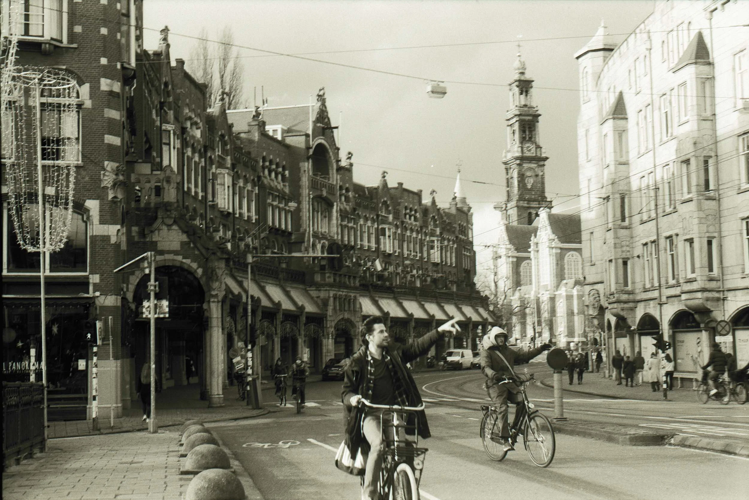 Stadscentrum met mensen op de fiets en wandelend, historische gebouwen en een toren in de achtergrond, herfstliggende bomen.