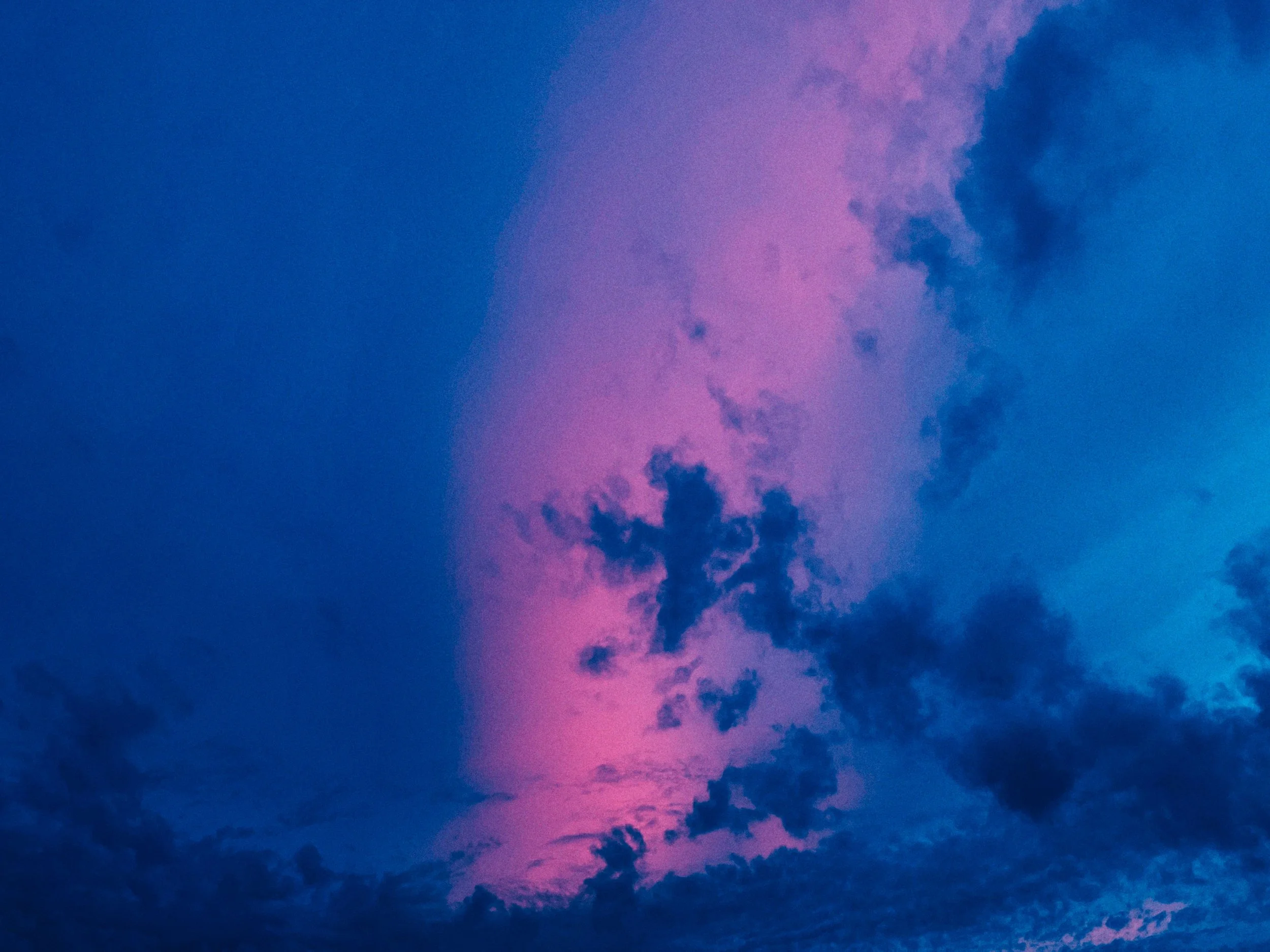 De lucht met roze, paarse en blauwe kleuren tijdens zonsondergang, met enkele donkere wolken.