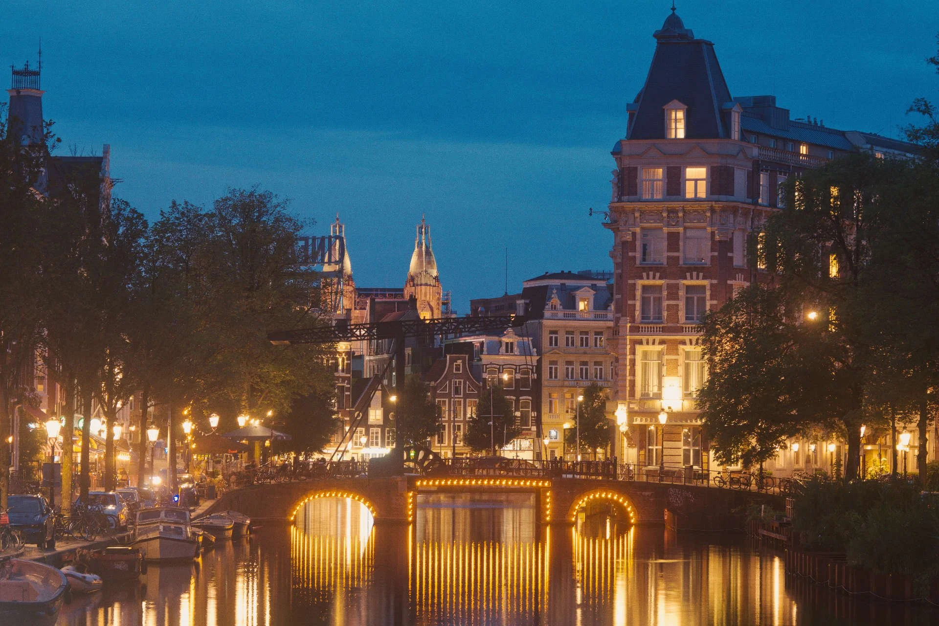 Een verlichte stad met historische gebouwen en een brug met gouden verlichting over een kanaal, 's avonds.