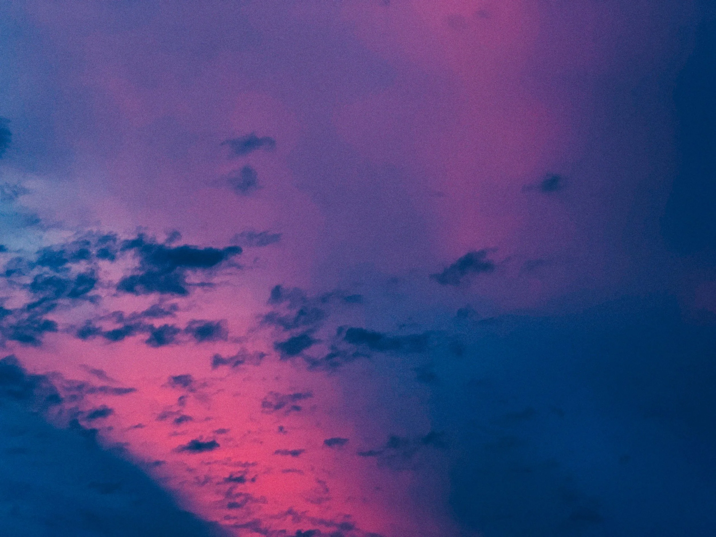 De lucht met een mengeling van roze, paarse en blauwe kleuren na zonsondergang, met verspreide donkere wolken.