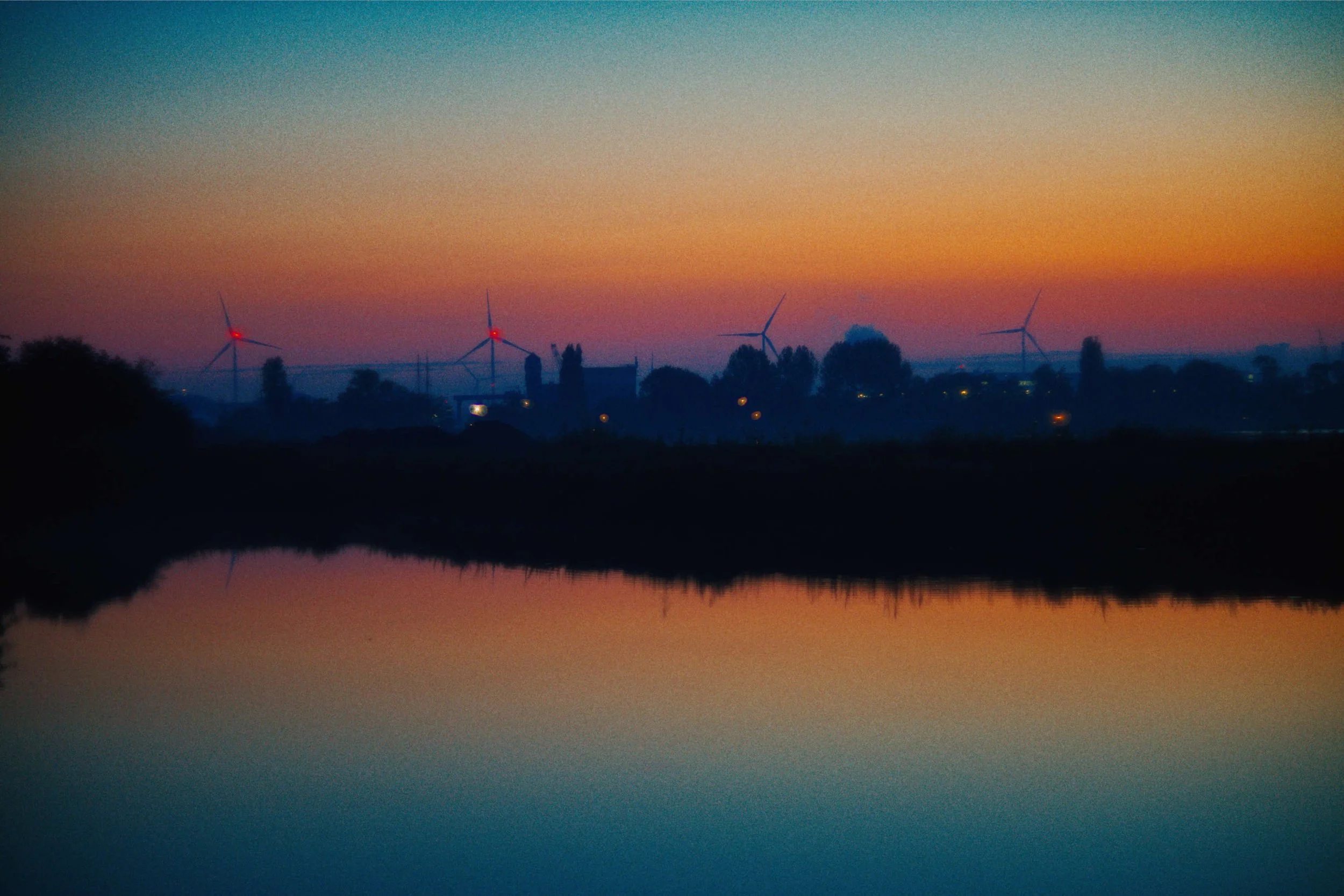 Een landschap met windturbines bij zonsondergang, weerspiegeling in het water.