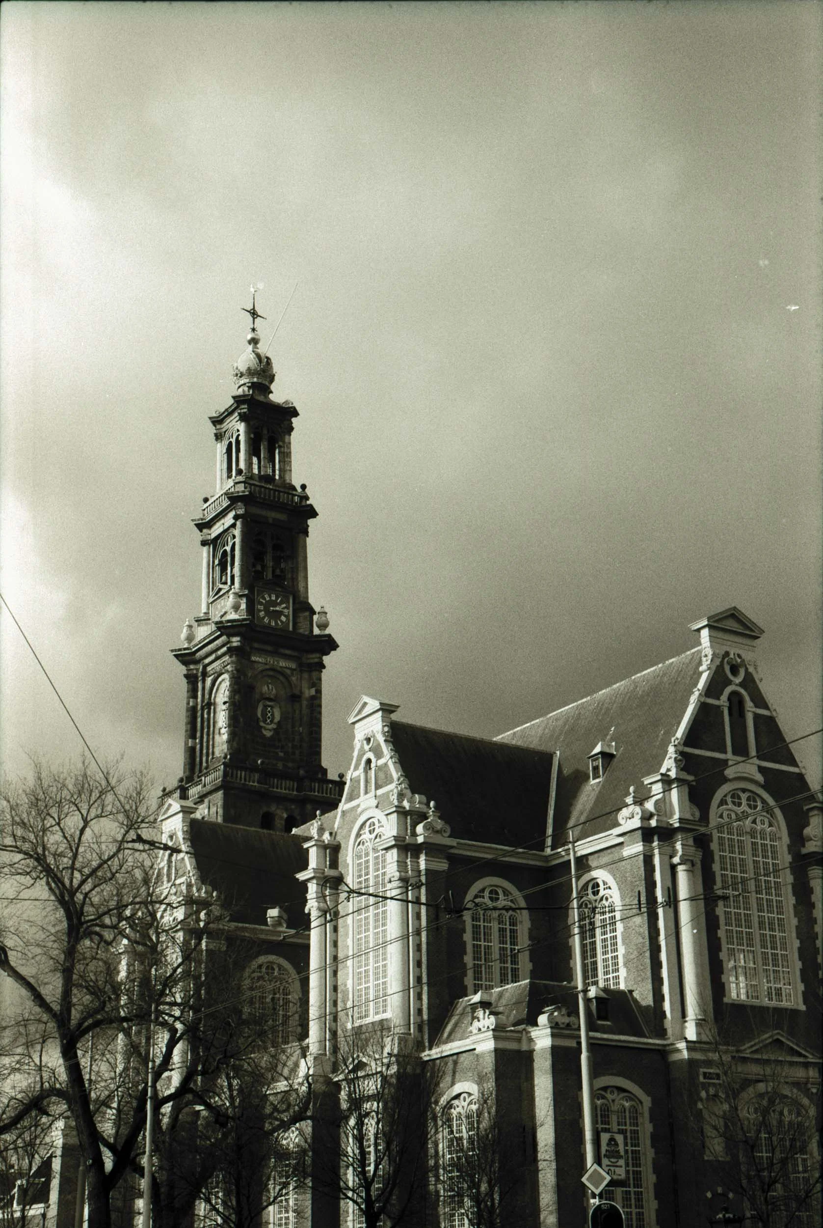 Een oude kerk met een hoge klokkentoren, omringd door enkele bomen en elektrische draden.