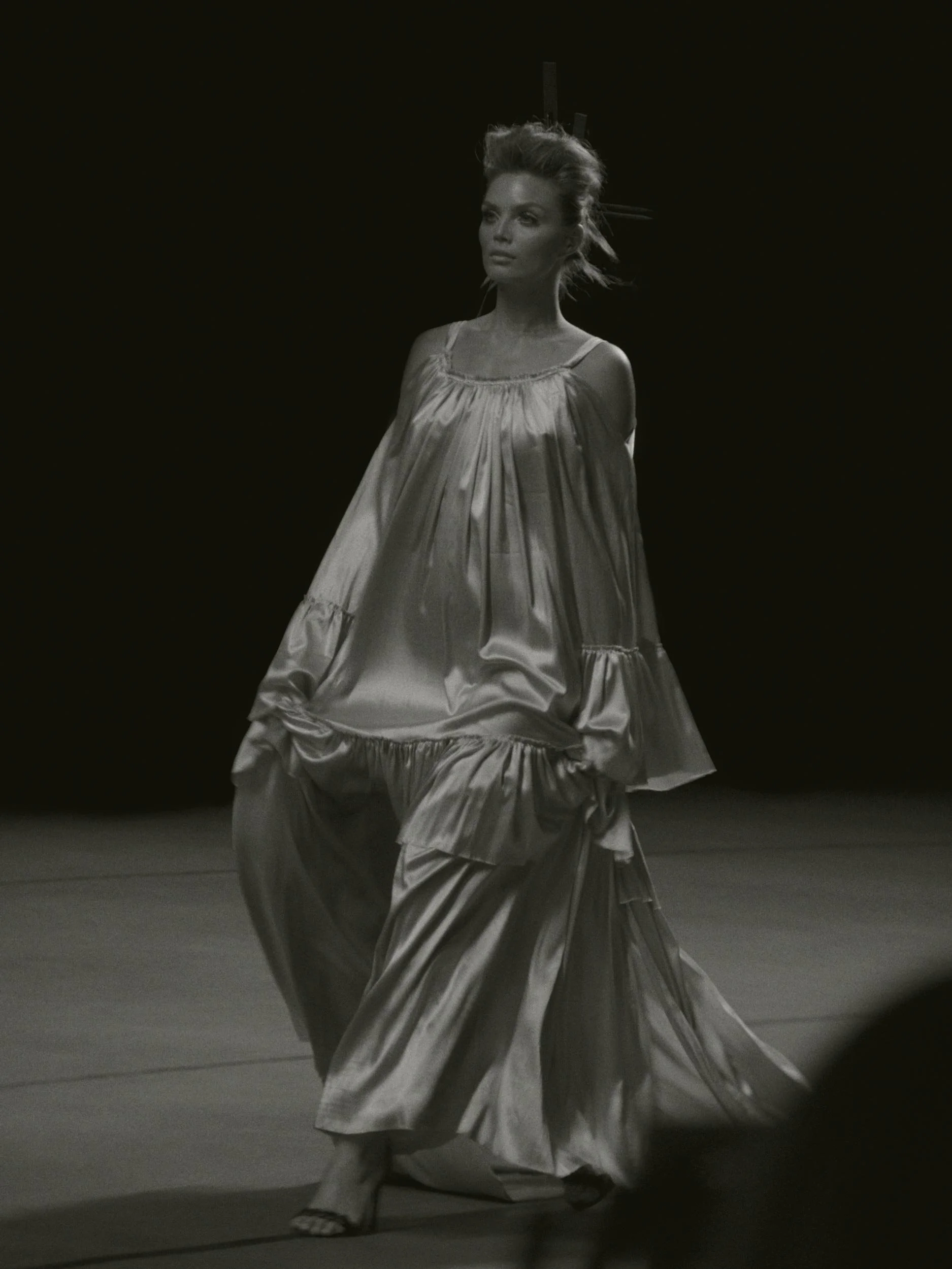 Zwart-wit foto van Kim Veenstra in een lang, glanzend jurk met kralen, op een podium of catwalk.