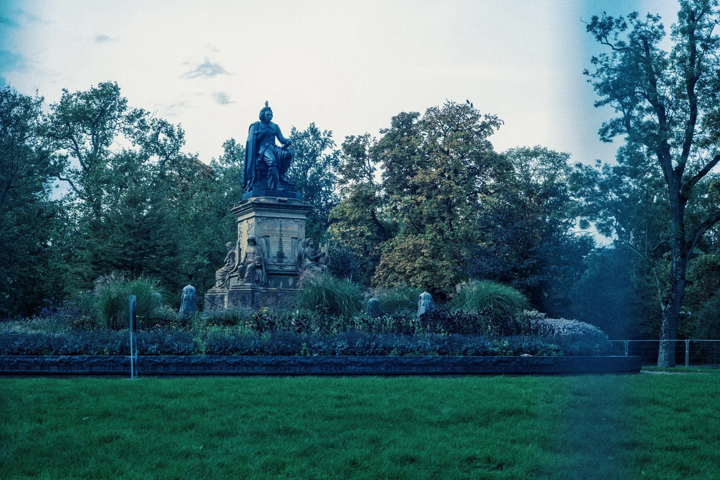 Een standbeeld in een park met veel bomen en groene grasvelden.