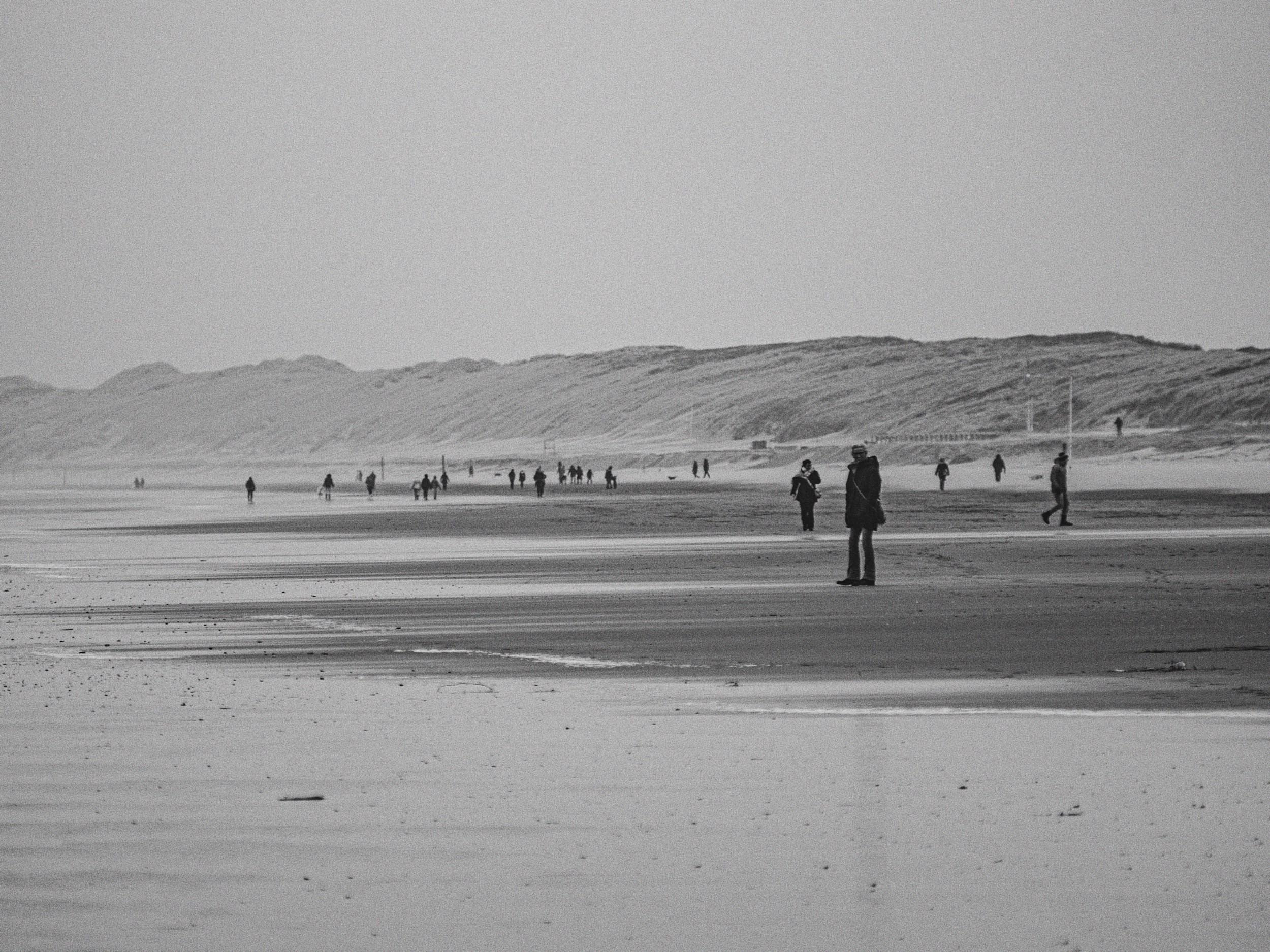 Zwaluwstrand met mensen die wandelen op het strand, een duinenlandschap op de achtergrond, in zwart-wit