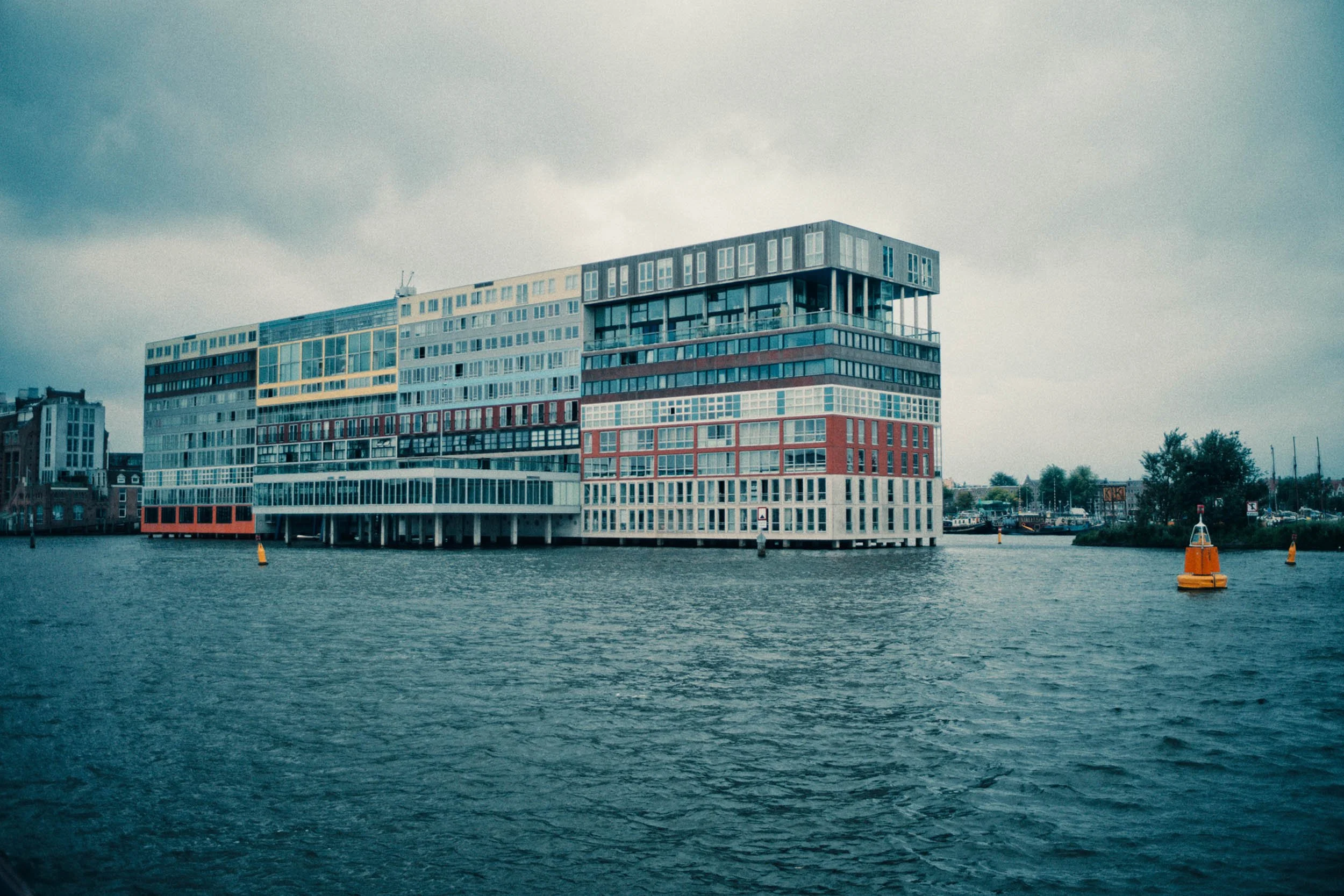 Moderne gebouw verbonden aan de waterkant met een waterweg voor de voorgrond en een bewolkte hemel boven.