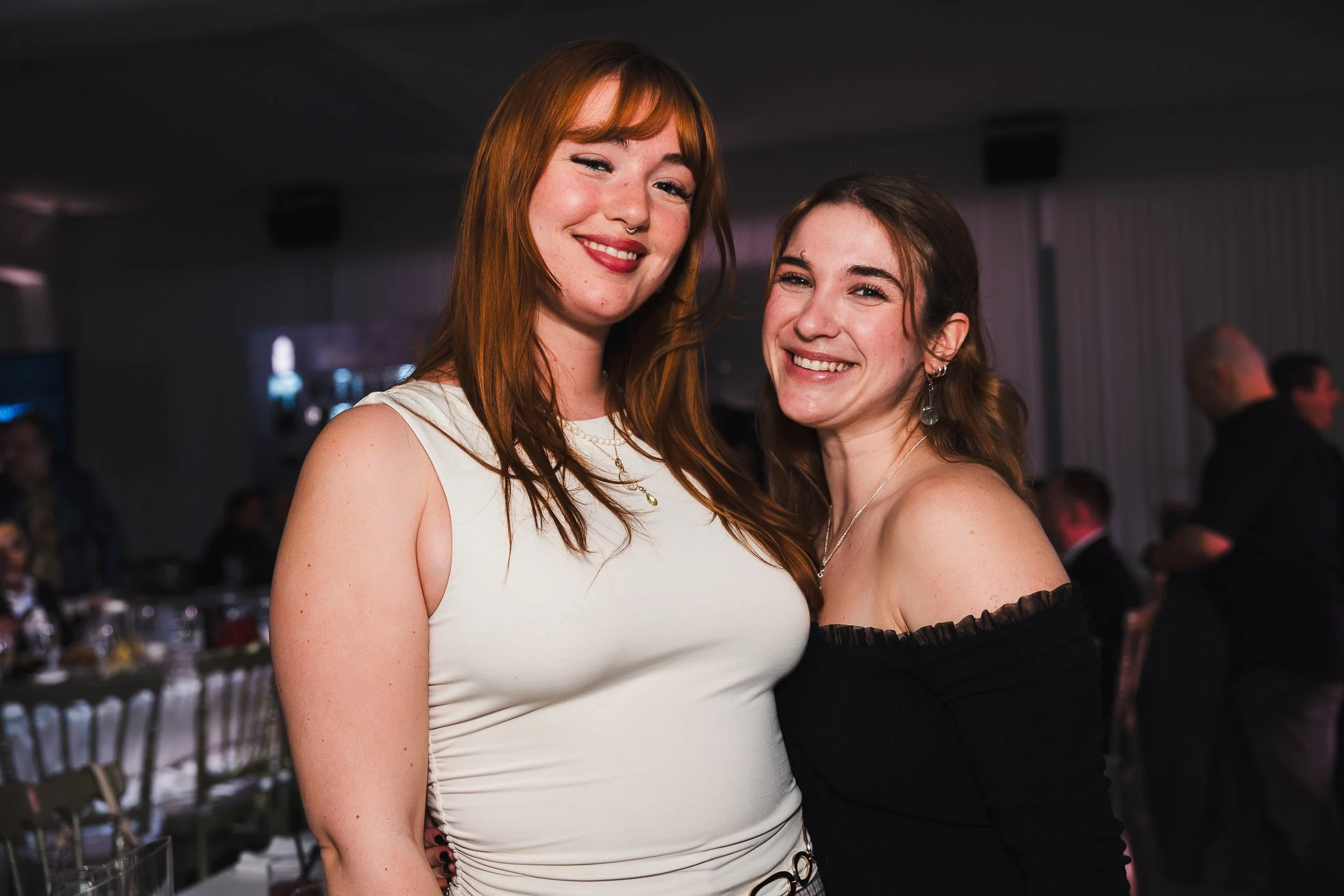 Deux jeunes femmes souriantes posant ensemble dans une ambiance de fête ou d'événement social.