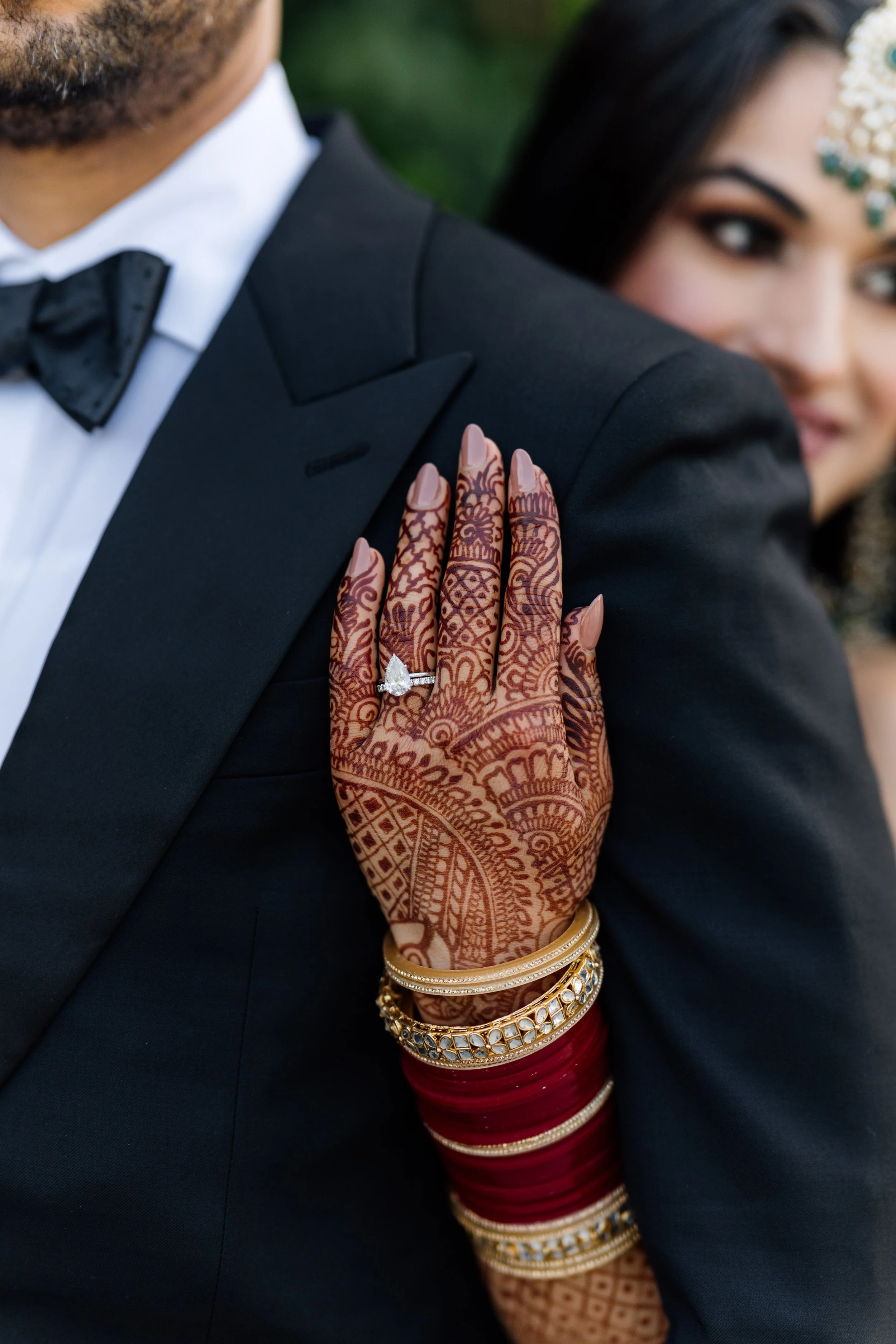 Bride standing behind groom with her henna-covered hand on his shoulder, capturing a refined fusion of tradition and modern elegance