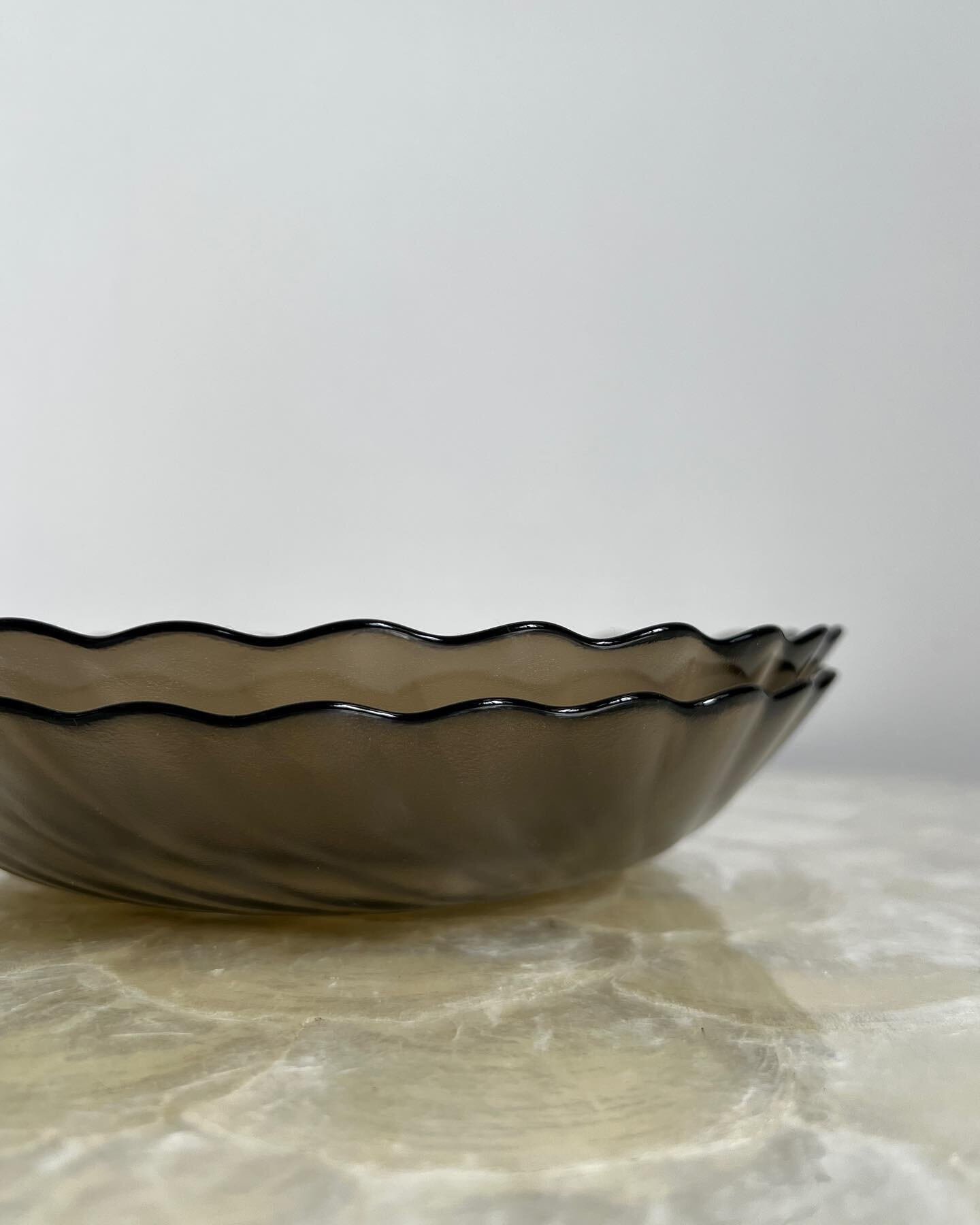 A set of two scallop-edged bowls in smoky glass. The underside of the bowls have a fine texture resulting in a matte finish, while the inside of the bowls have a smooth glossy finish. Not many were produced, making these bowls rare and hard to come b