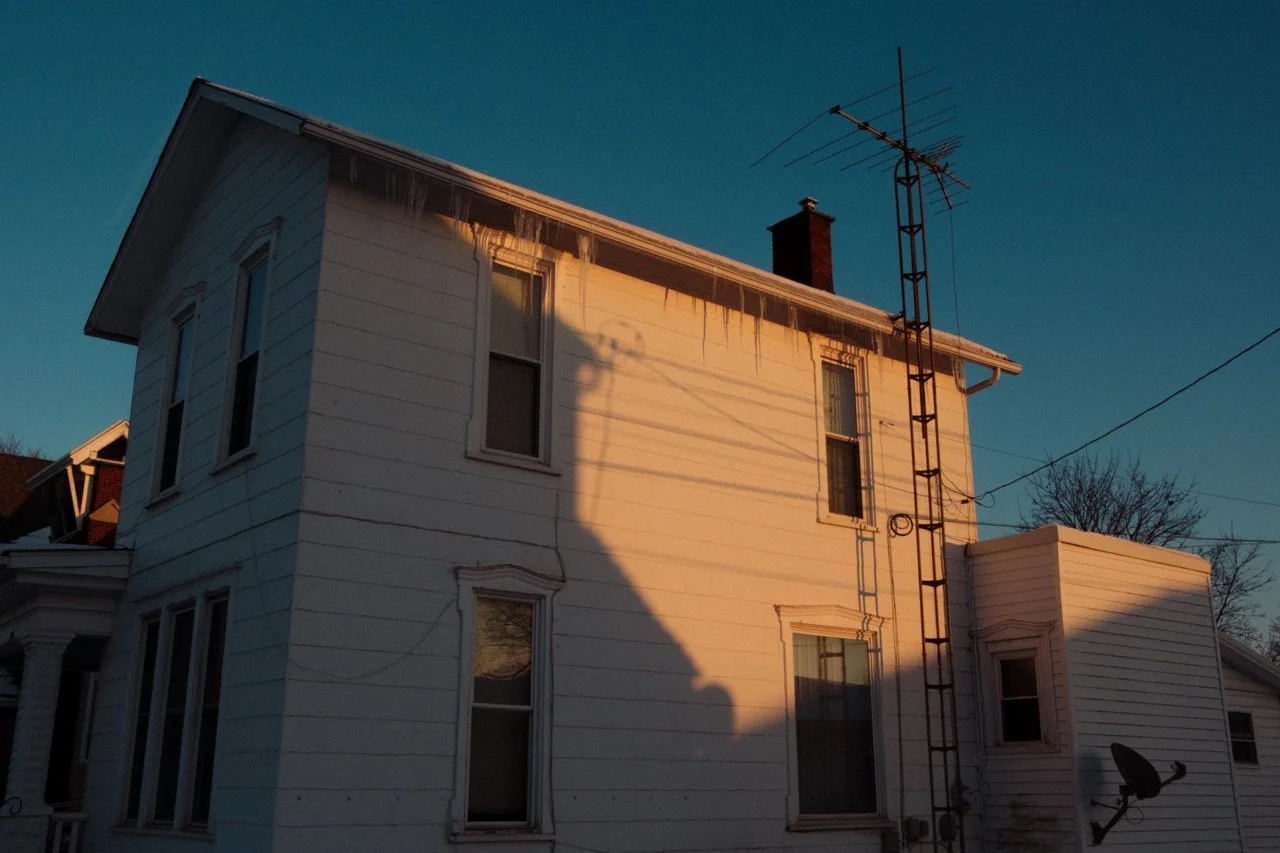 Sunset illuminating a two-story white house with icicles hanging from the roof and an old TV antenna on the roof.
