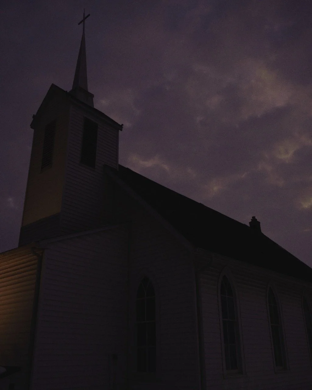 A silhouette of a church with a steeple topped by a cross, set against a dark, cloudy night sky.