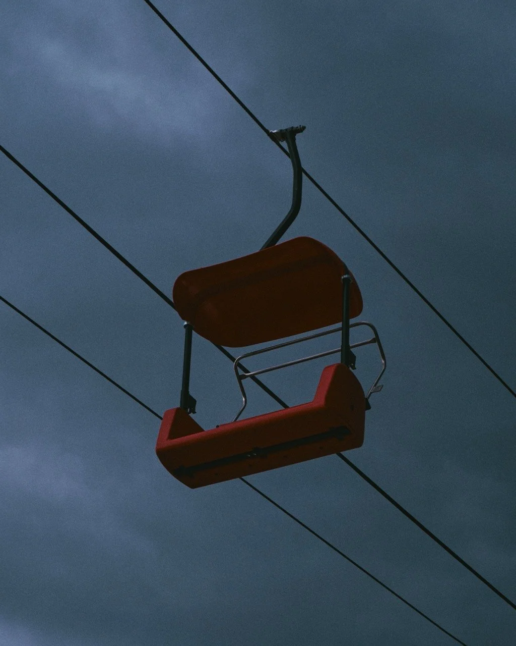 Empty chairlift seat hanging from cable against a cloudy sky at dusk or dawn.