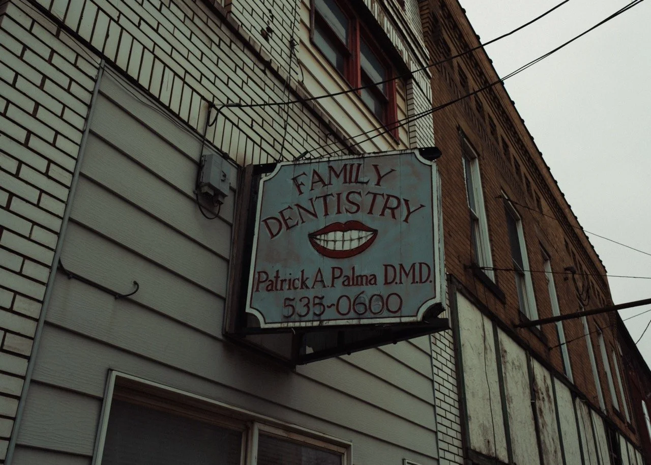 Sign for a family dentistry office with a drawing of a smiling mouth, located on a building with beige siding and brick exterior.