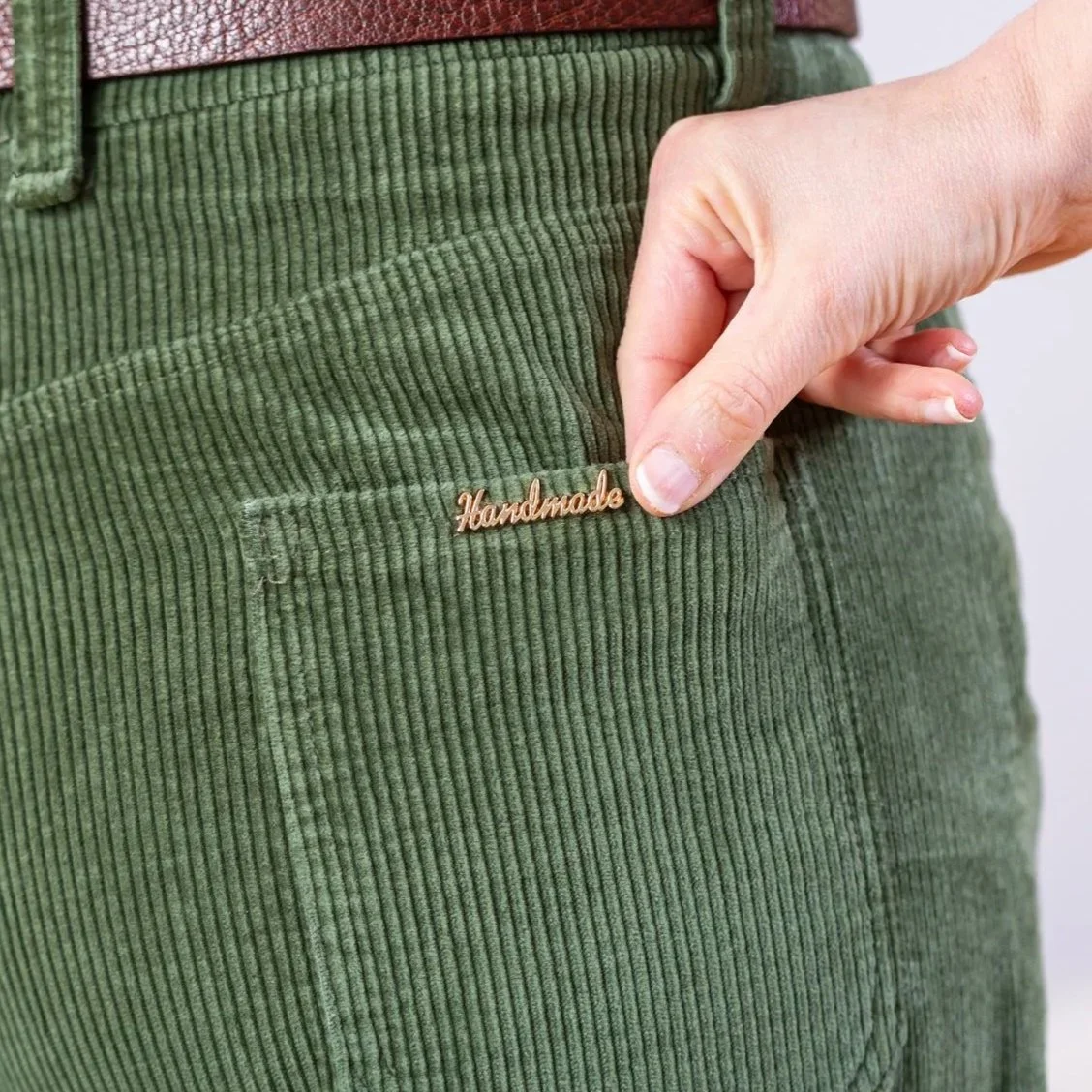 Detail of a pair of corduroy trousers back pocket with a metal label that says 'handmade'.