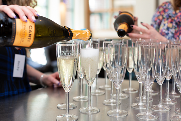Prosecco being poured into fluted glasses during afternoon tea at a social sewing day.