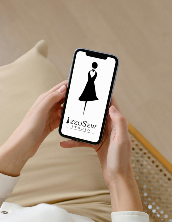 A person holding a smartphone displaying the IzzoSew Studio logo, featuring a minimalist black dress form icon, representing the accessibility of the new online sewing video subscription.
