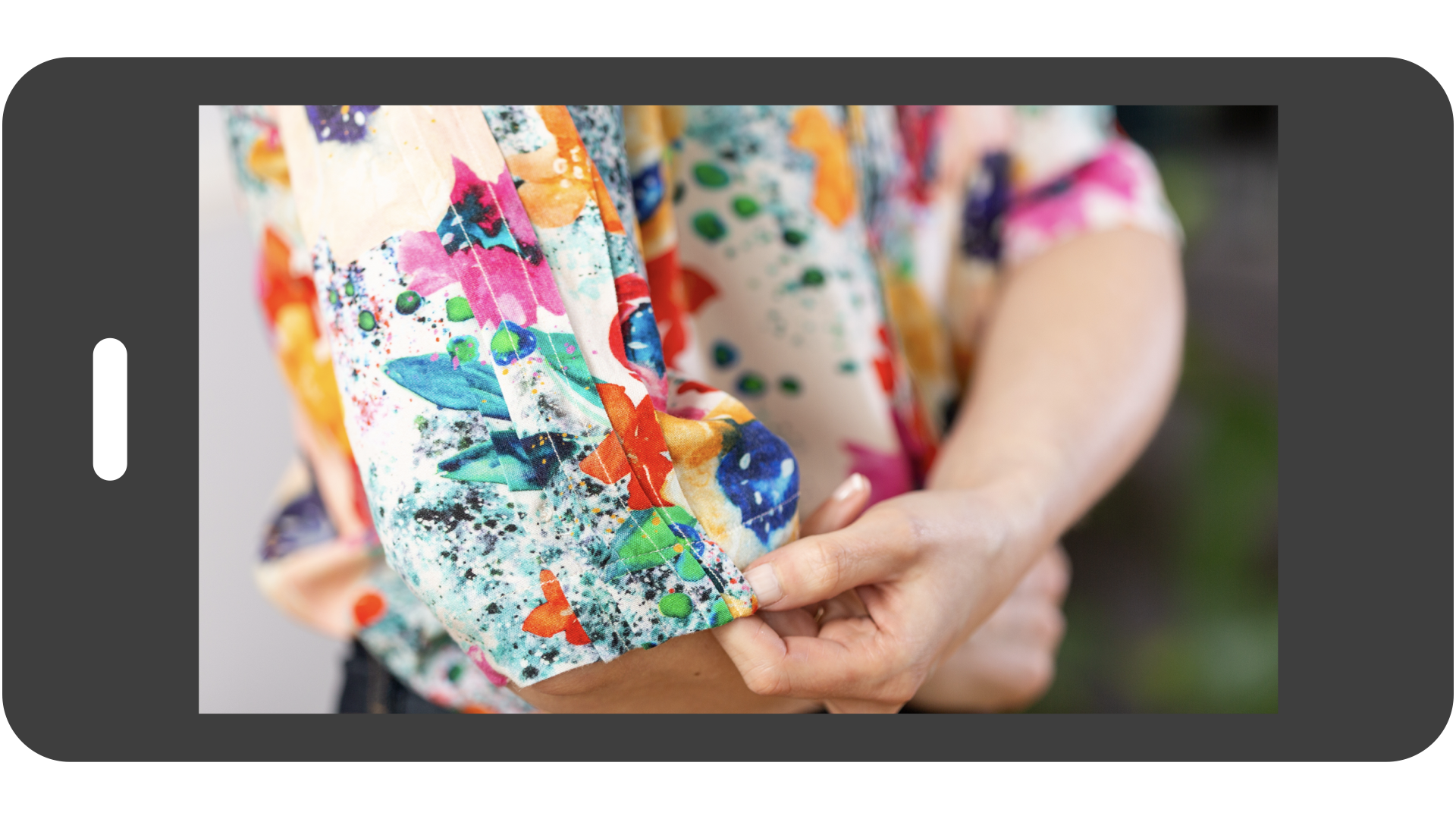 A digital smartphone preview of a technical sewing lesson, featuring a close-up of a hand adjusting a precise triple-pleat detail on the cuff of a vibrant, floral-print handmade blouse.