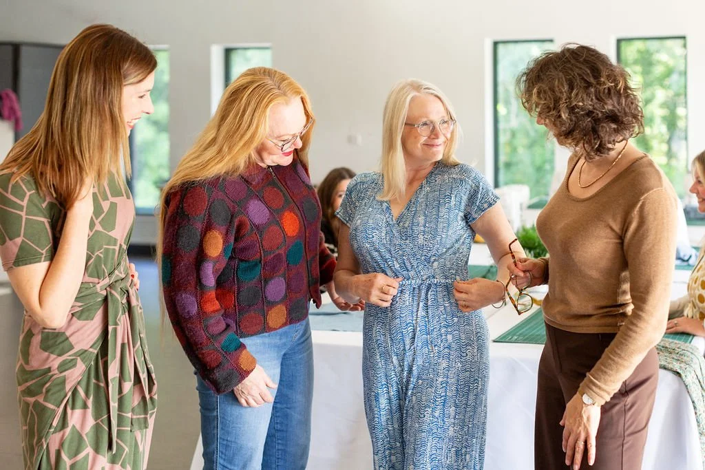 Three women showing thier homemade garments to each other, smiling and looking friendly.