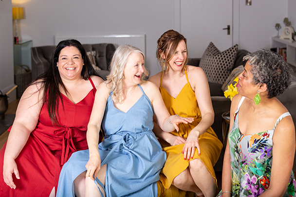 Female models sitting on a sofa wearing the Dovestone Dress by IzzoSew Studio.