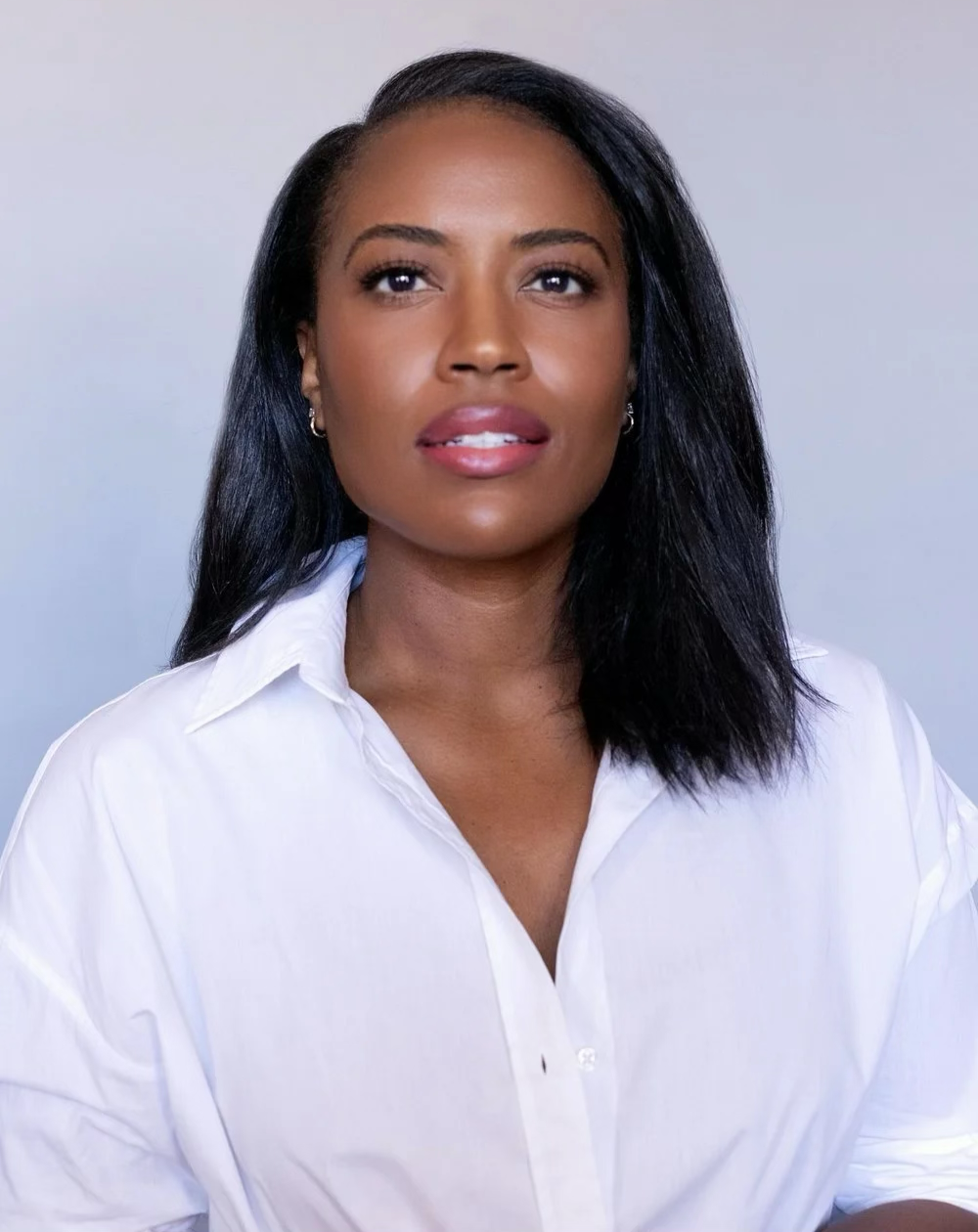 Portrait of a woman with dark hair, wearing a white collared shirt, against a neutral background.