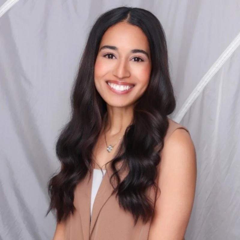 A woman with long dark hair smiling at the camera in a black shirt, in a well-lit indoor setting.