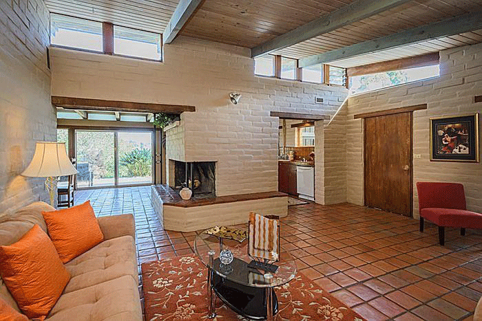 The living room of the existing property showing white brick wall, tile flooring and warm orange and red tones
