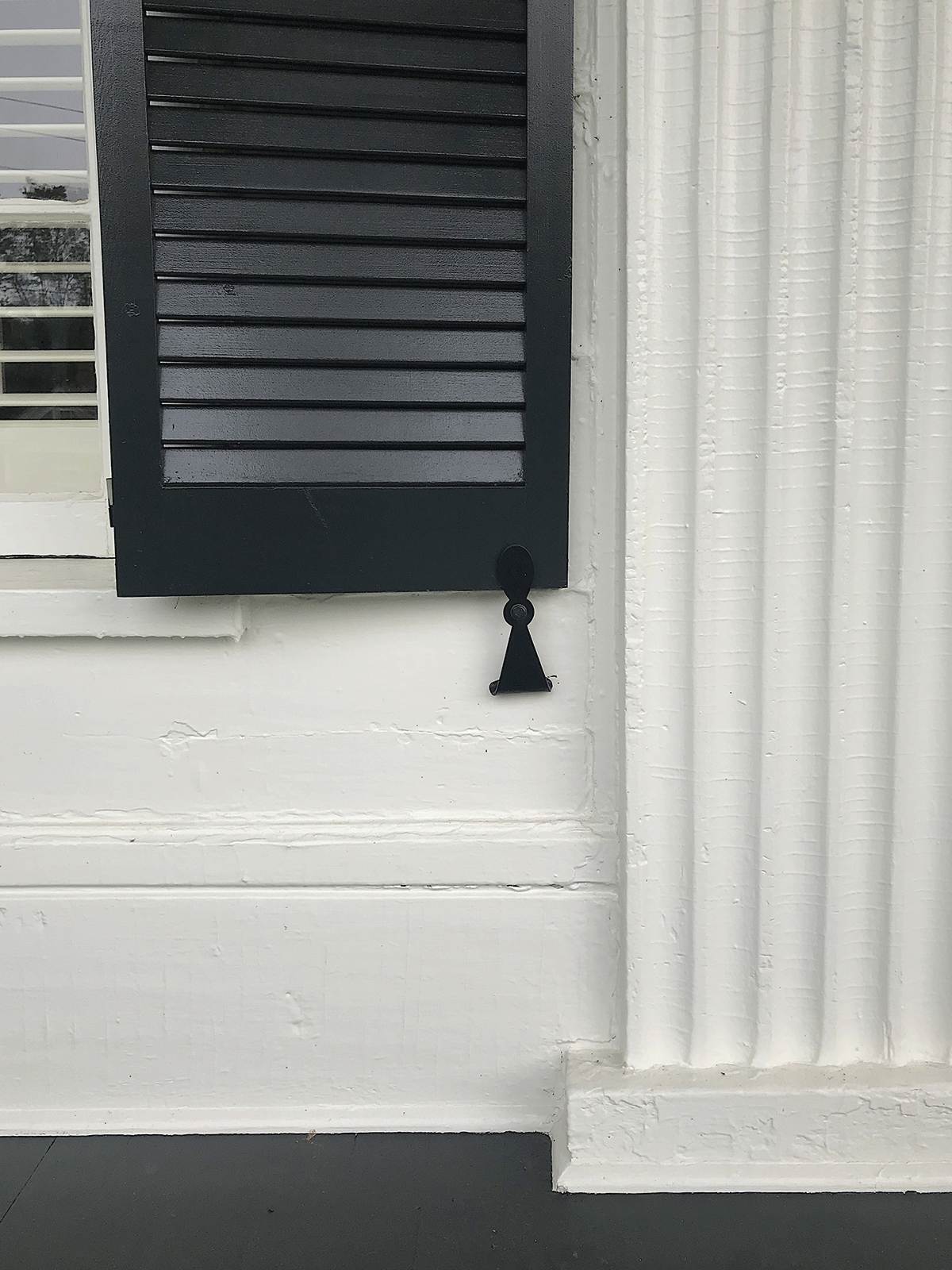 A picture of a dark shutter on a porch window with focus on the hardware detail
