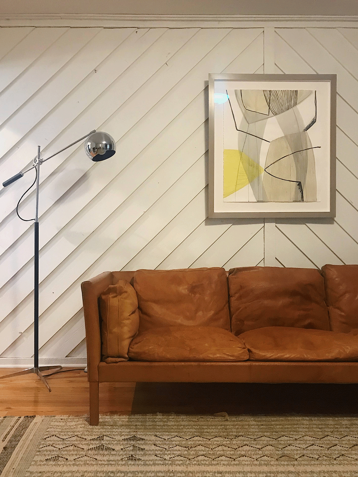 A leather sofa against a wall with a wooden chevron pattern, next to a lamp