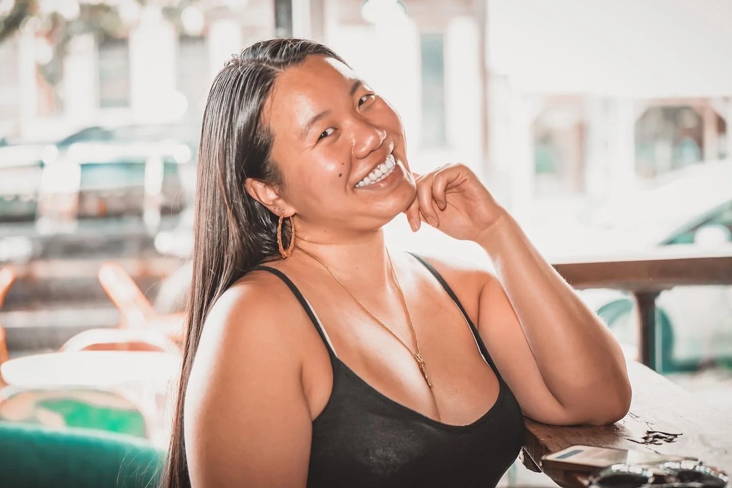 Smiling woman sitting at a table in a cafe with a window in the background.