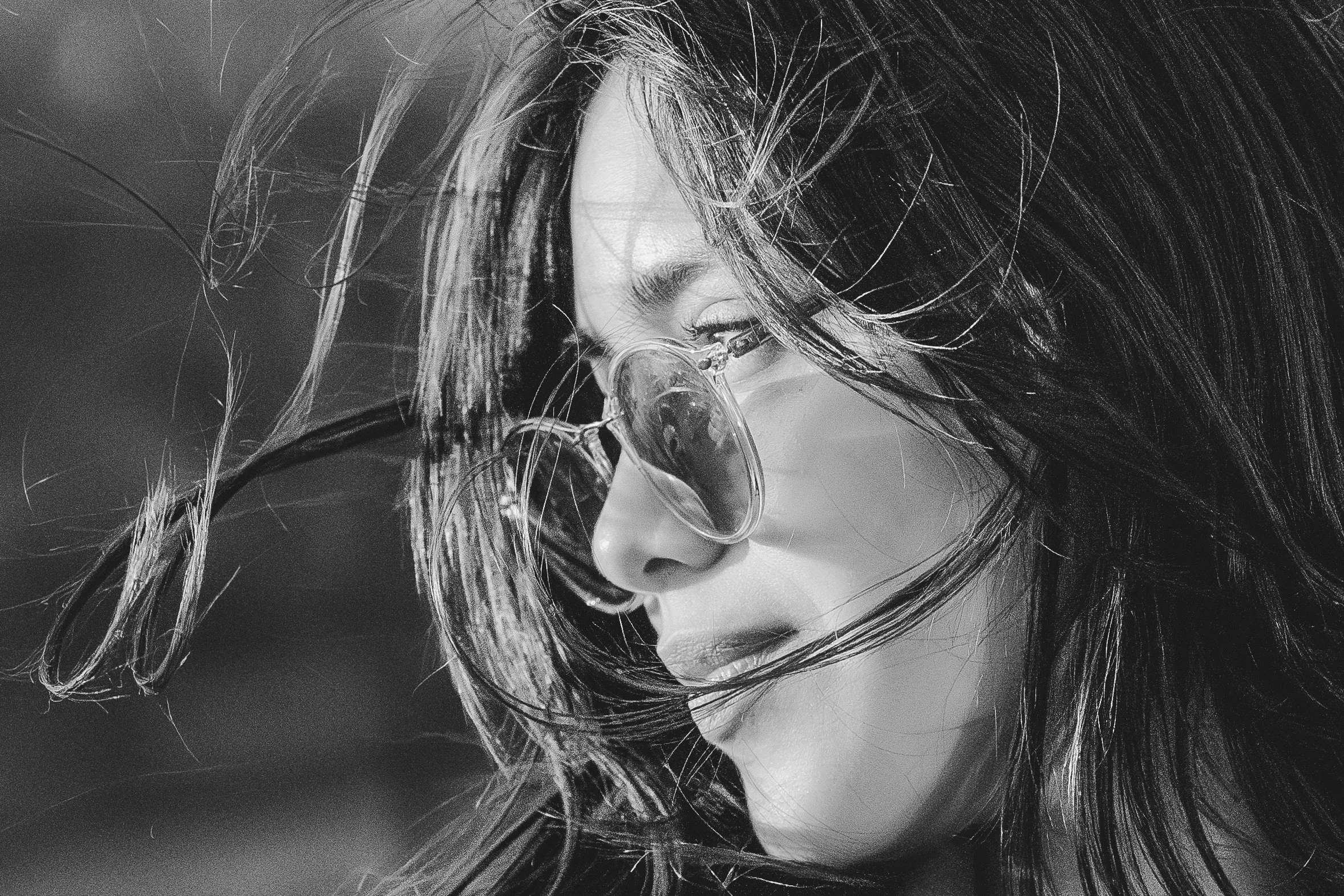 Black and white portrait of a woman wearing sunglasses, with hair blowing in the wind.