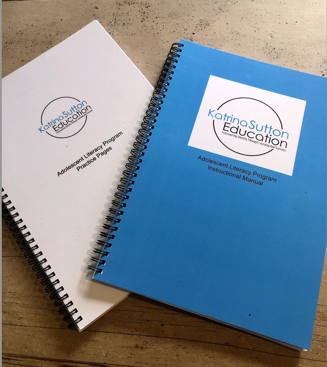 Two spiral-bound booklets on a wooden surface, one white titled 'Adolescent Literacy Program Practice Pages' and the other blue titled 'Adolescent Literacy Program Instructional Manual,' both with the Katrinasutton Education logo.