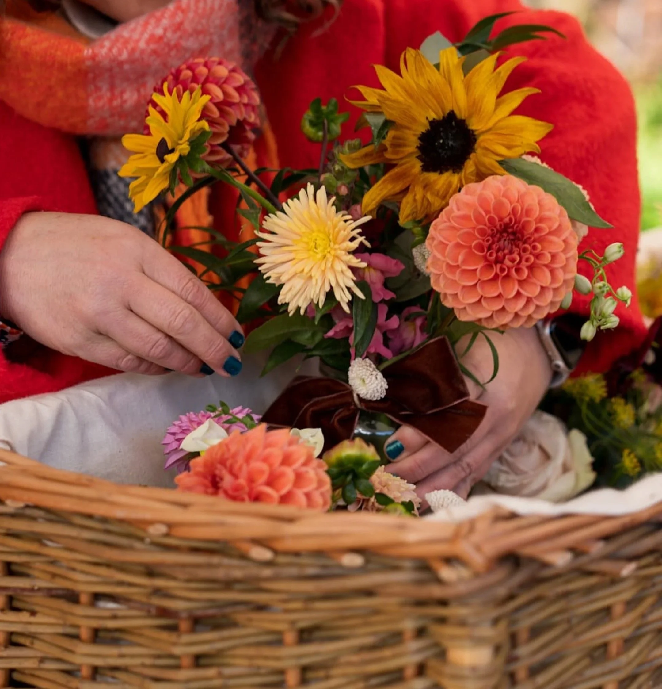 A woman's hands placing a vase of bright autumnal flowers into a wicker coffin