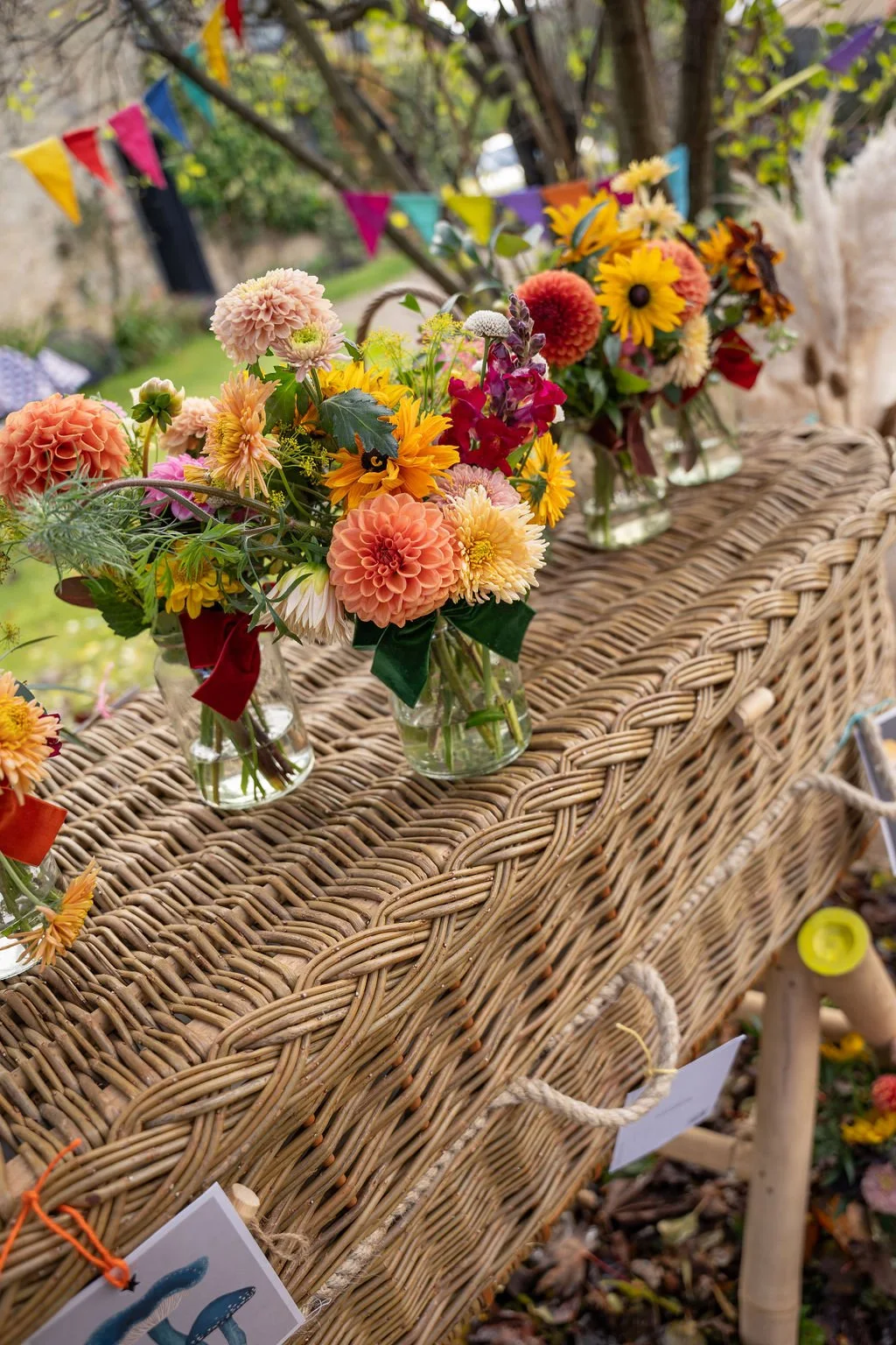 A row of vases of bright coloured autumnal flowers tied with velvet ribbons sitting on top of a closed wicker coffin