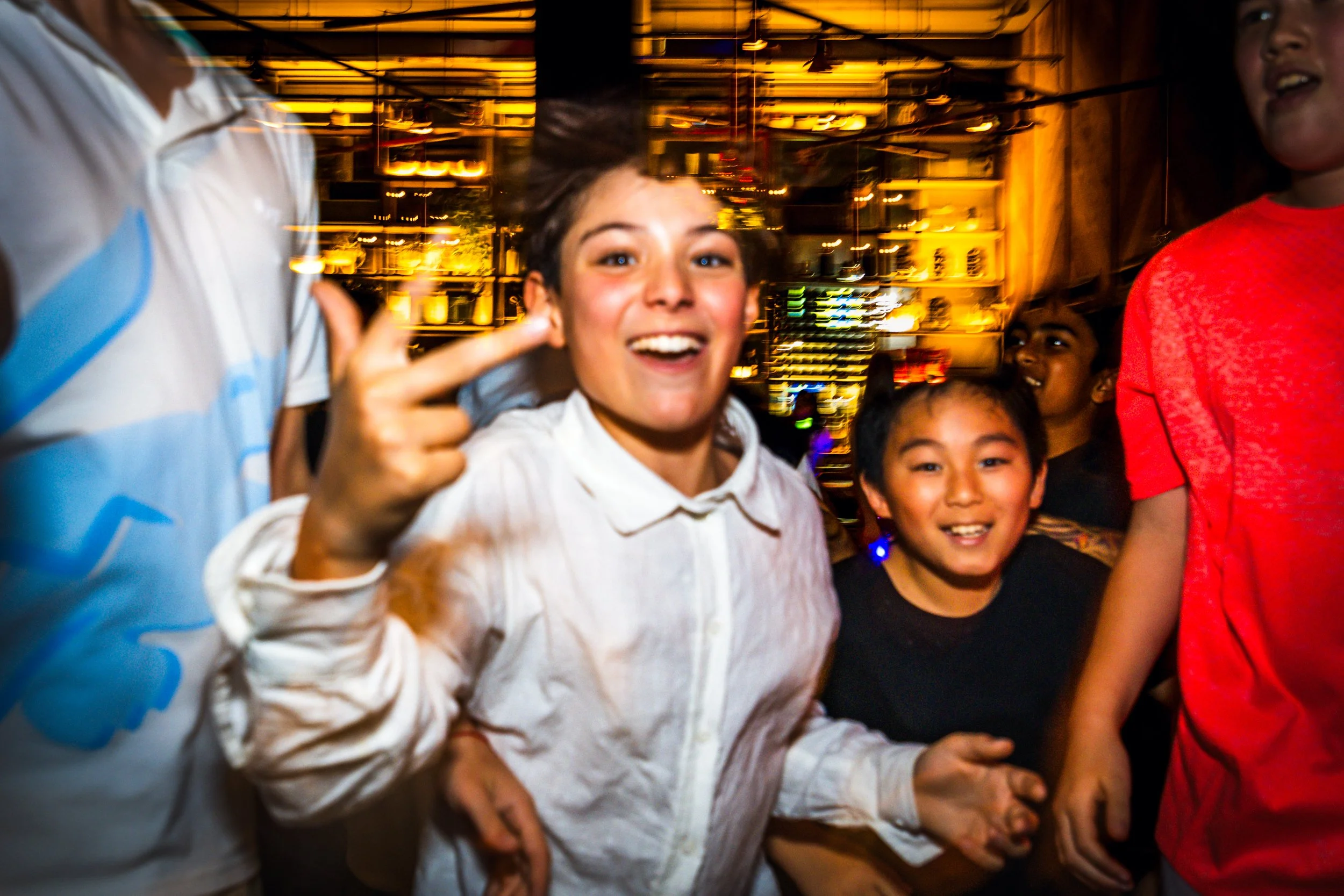 Group of children smiling and enjoying themselves in a lively indoor setting with a warm, ambient background.