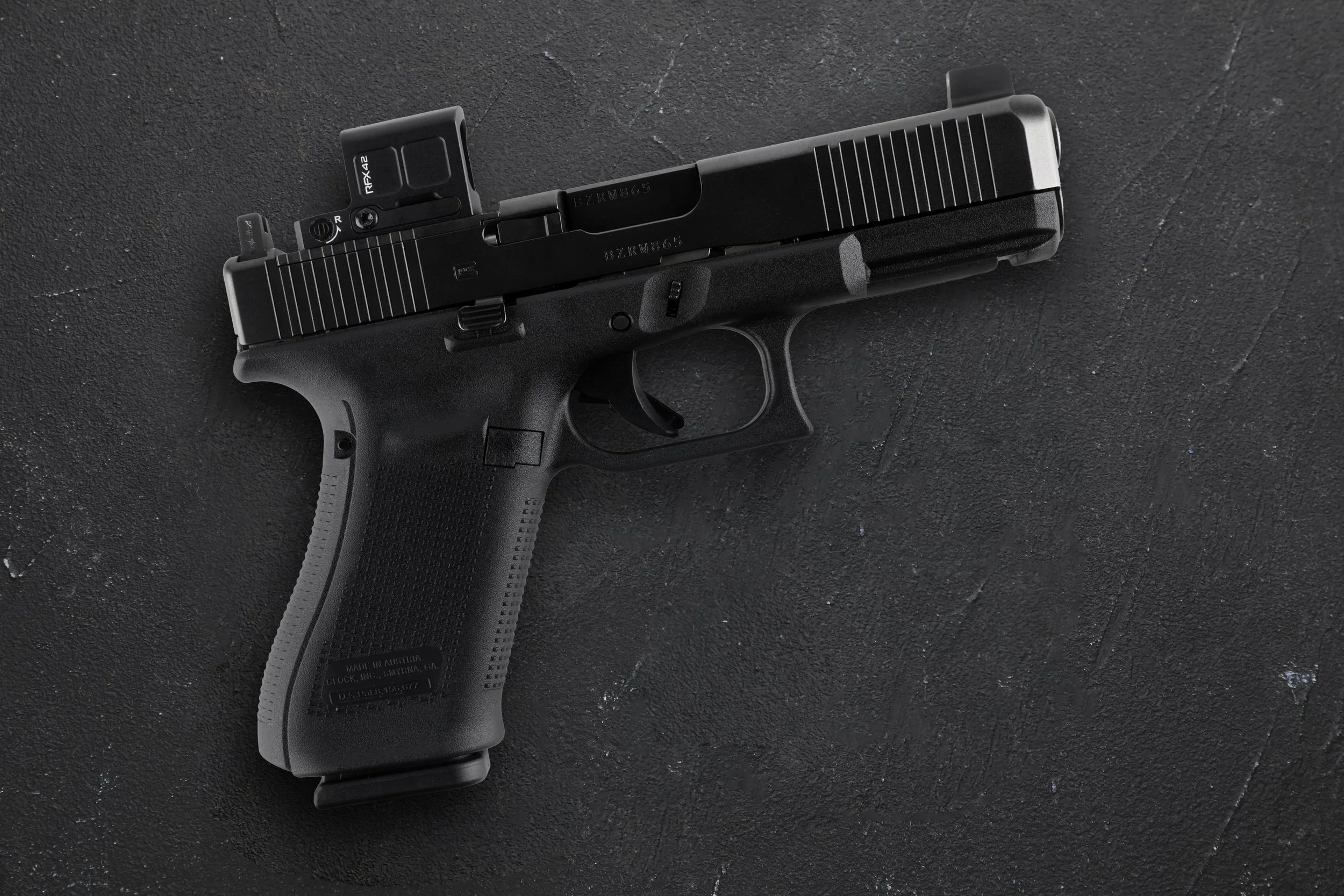 Black handgun with a mounted optic on a dark textured background.