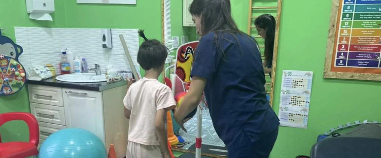 Tea, a Tek Ura physiotherapist, guiding a child through a balance exercise in the Durrës clinic