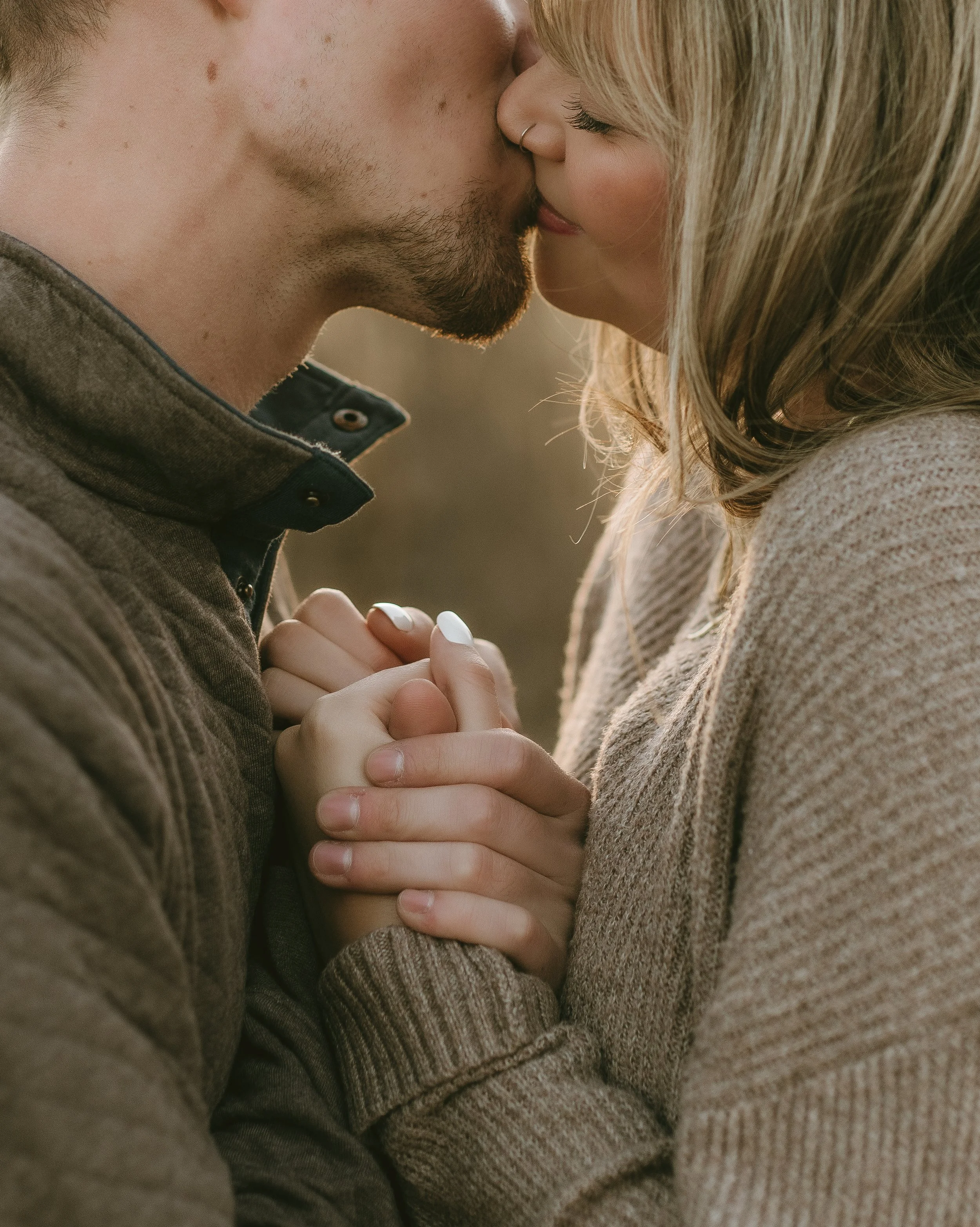 A close-up of a couple kissing, holding hands with fingers intertwined, during sunset.
