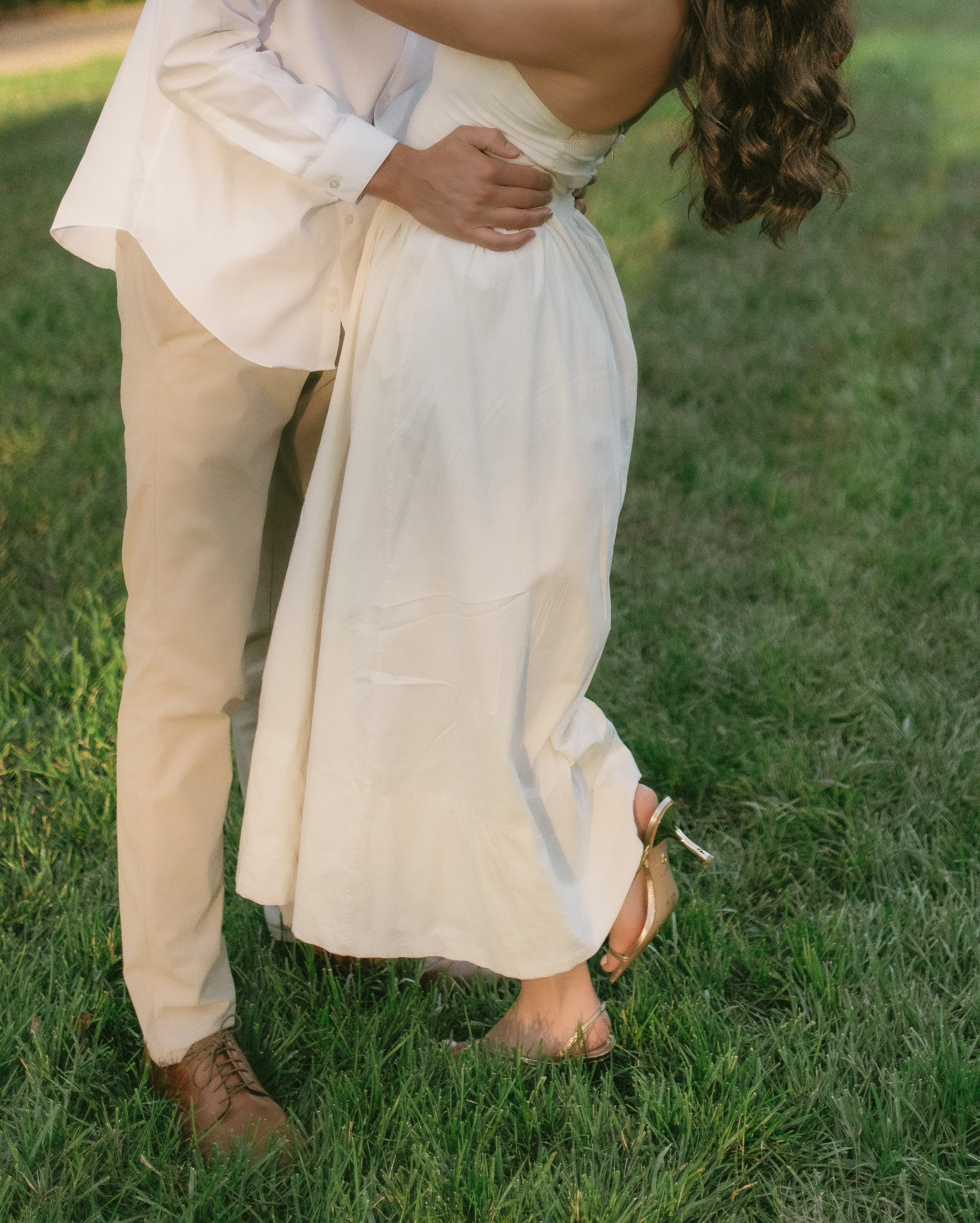 A couple in wedding attire embracing on a grassy field, with only part of their bodies visible.