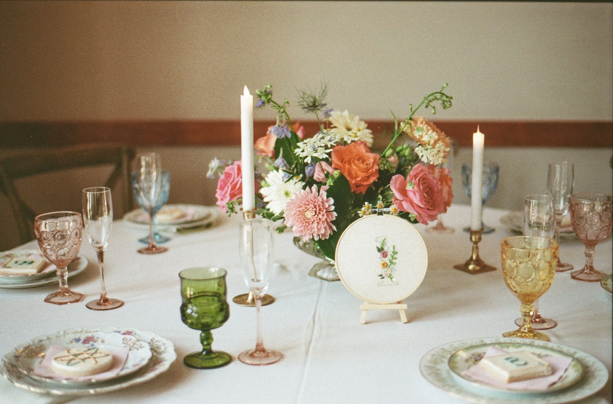 A table decorated with a floral centerpiece, candles, glassware, and plates, set for a meal or celebration.