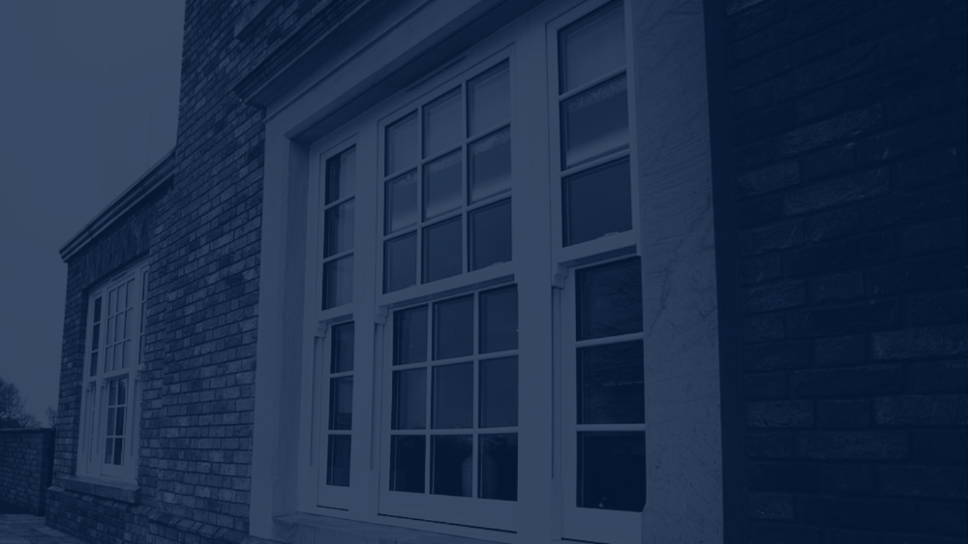 Blurred photo of a glass and metal greenhouse structure with trees and sky visible in the background.