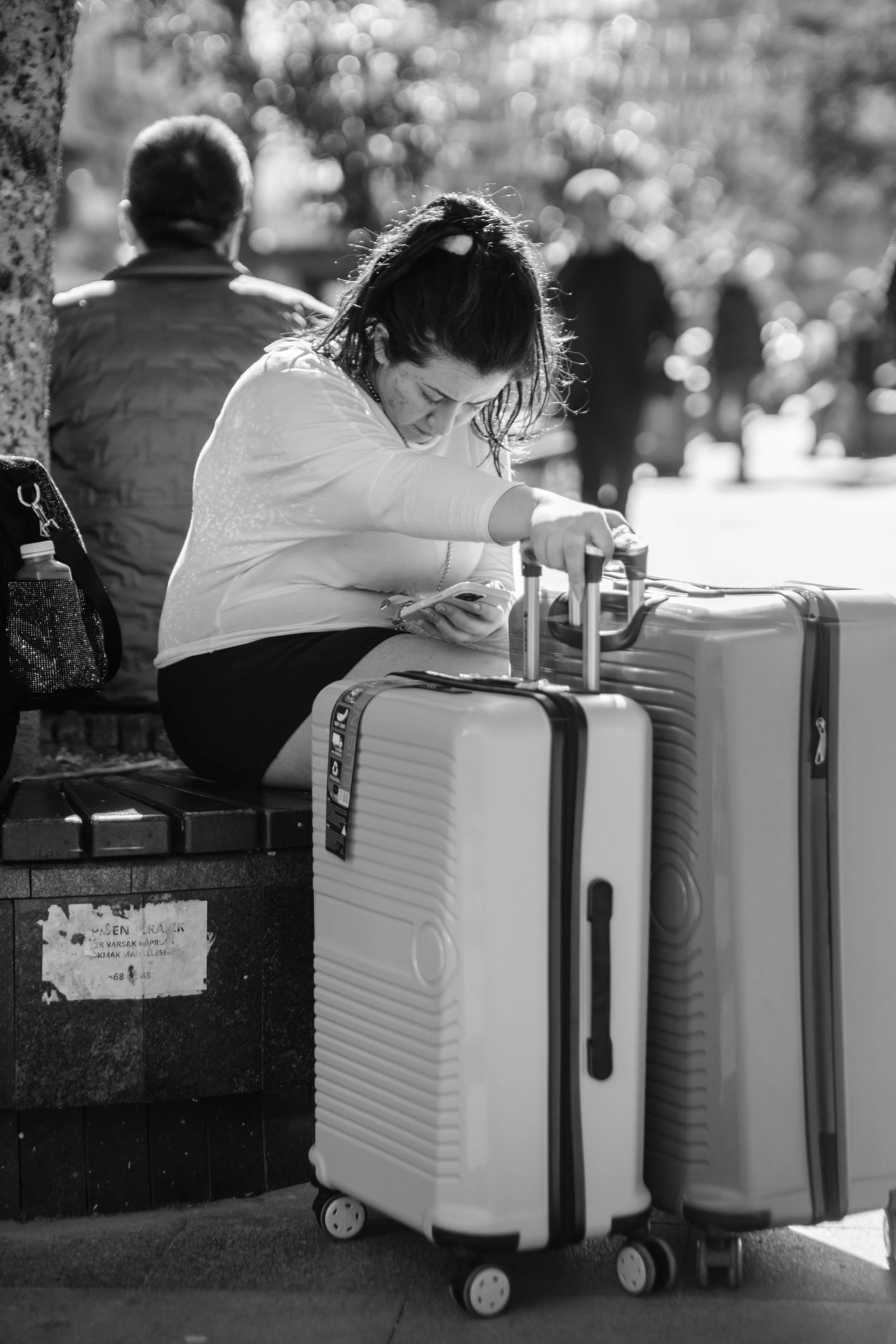 A woman sits in a city square with her suitcases, preparing for her journey.