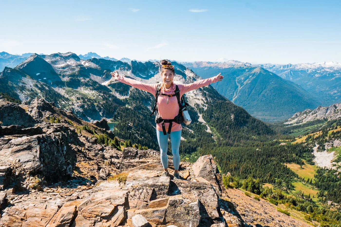 a woman hiker on the summit of a rocky peak with mountains in the background