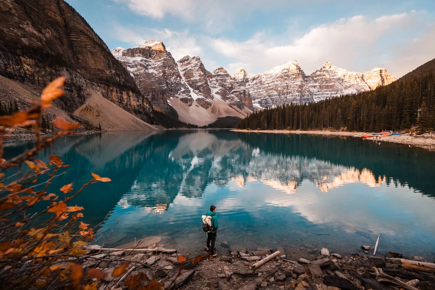 a hiker standing at the shore of a blue, reflective moraine lake in banff