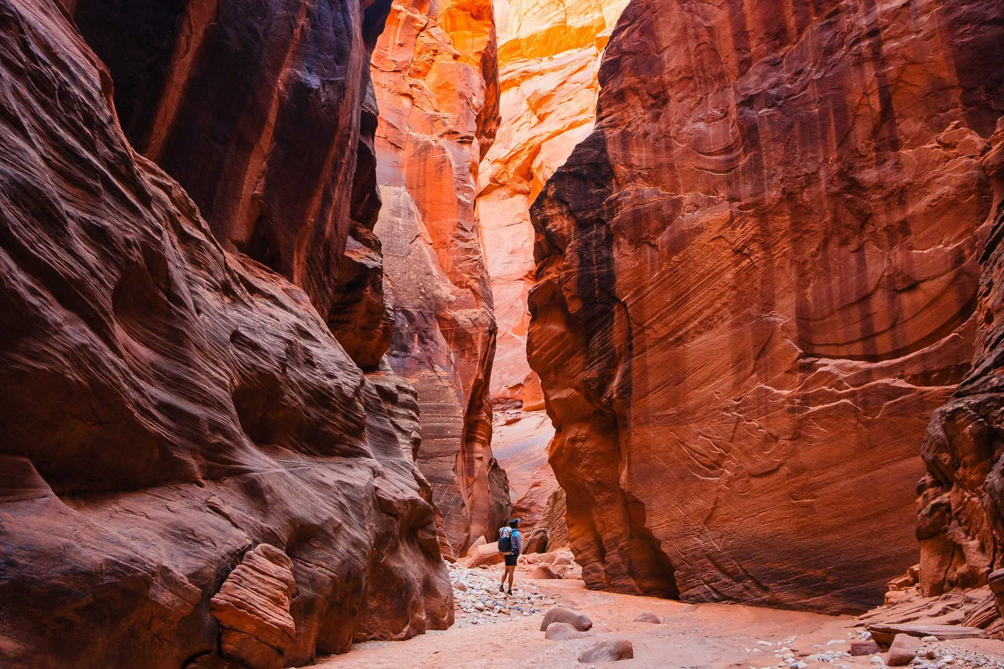 a tiny backpacker hiking through a slot canyon section of buckskin gulch with towering sandstone walls on either side