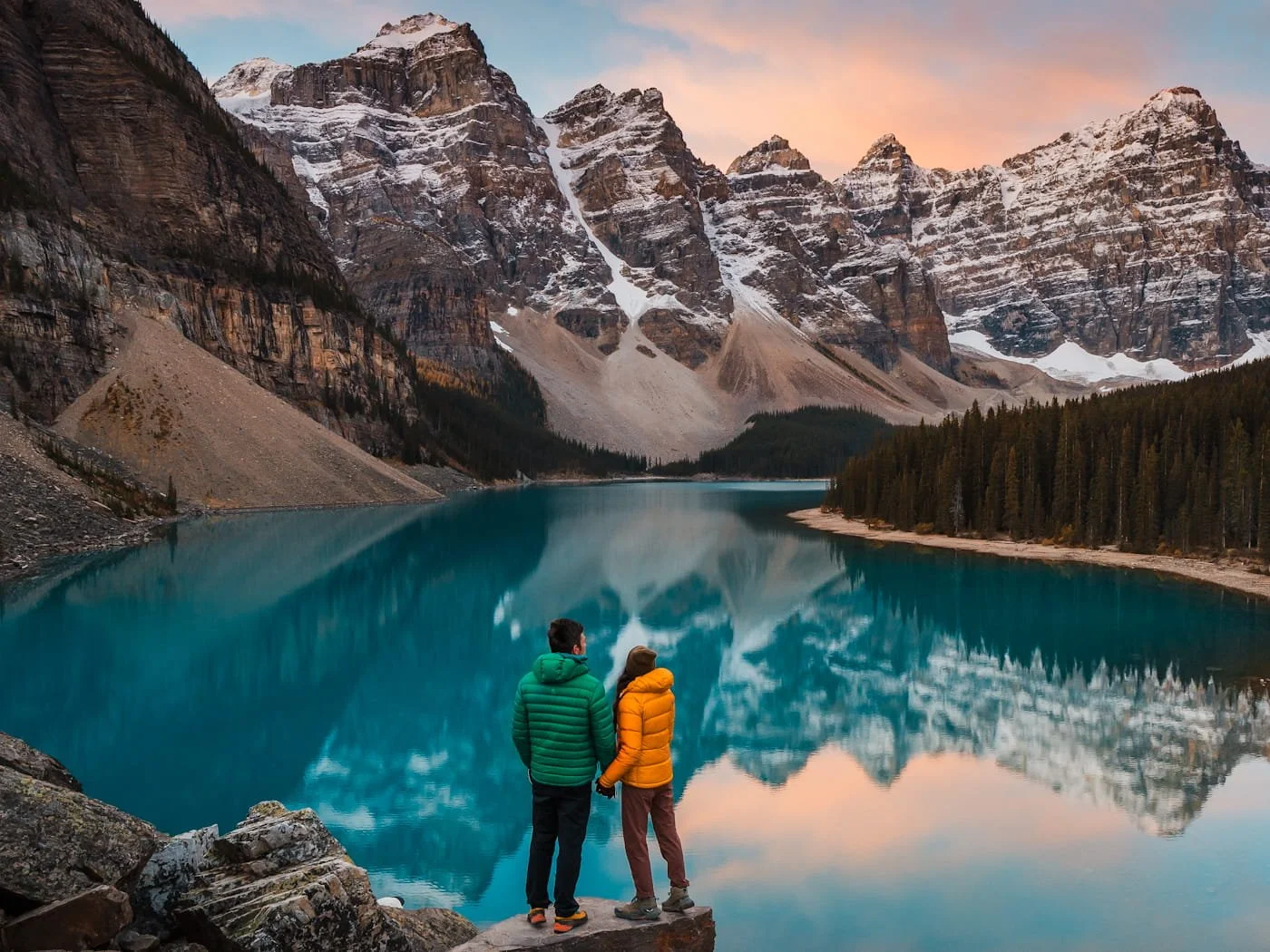 a couple standing on a rock overlooking a bright blue moraine lake and mountains in Banff