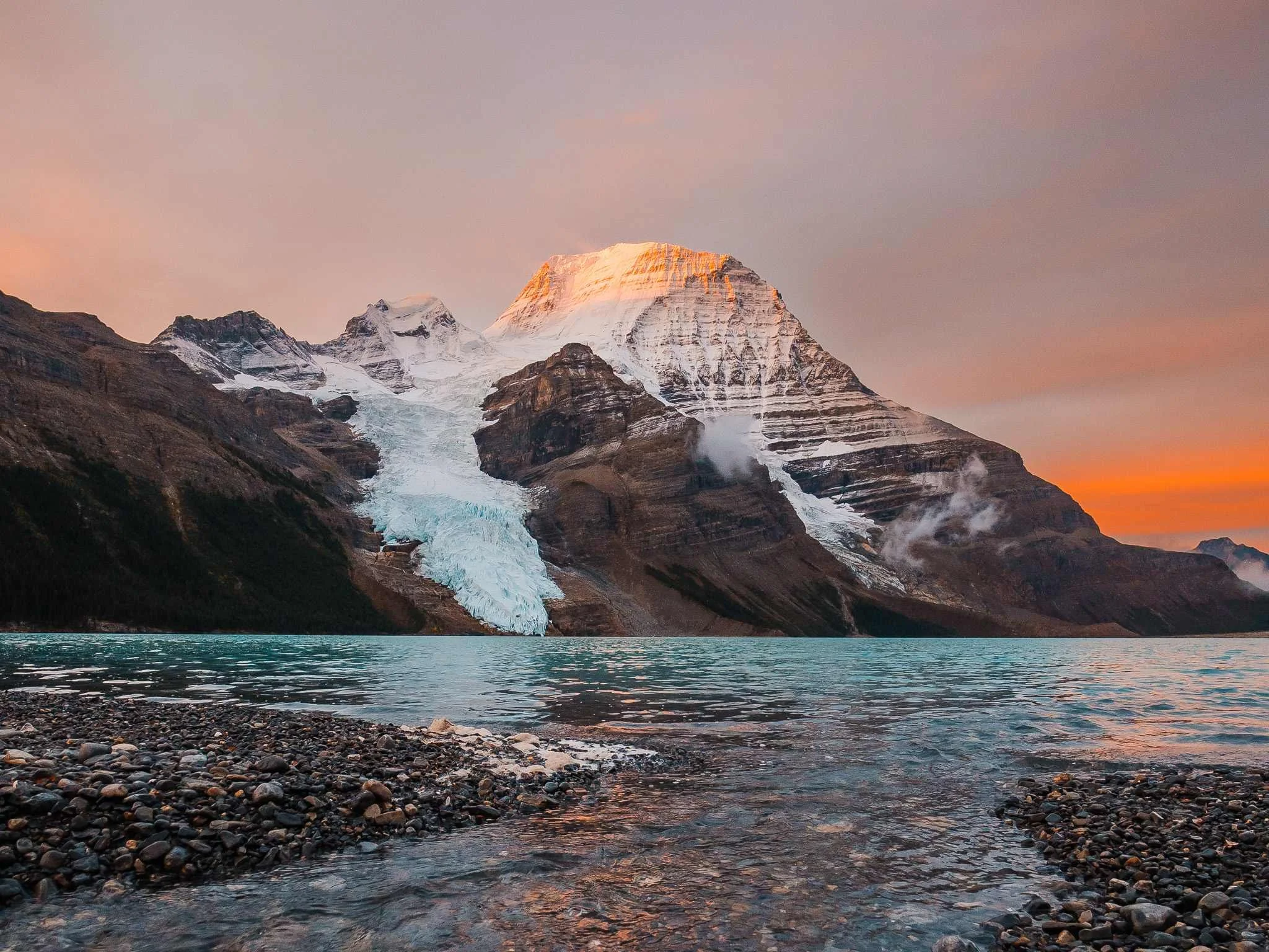 sunrise with pink alpinglow and blue water with a glaciated mountain